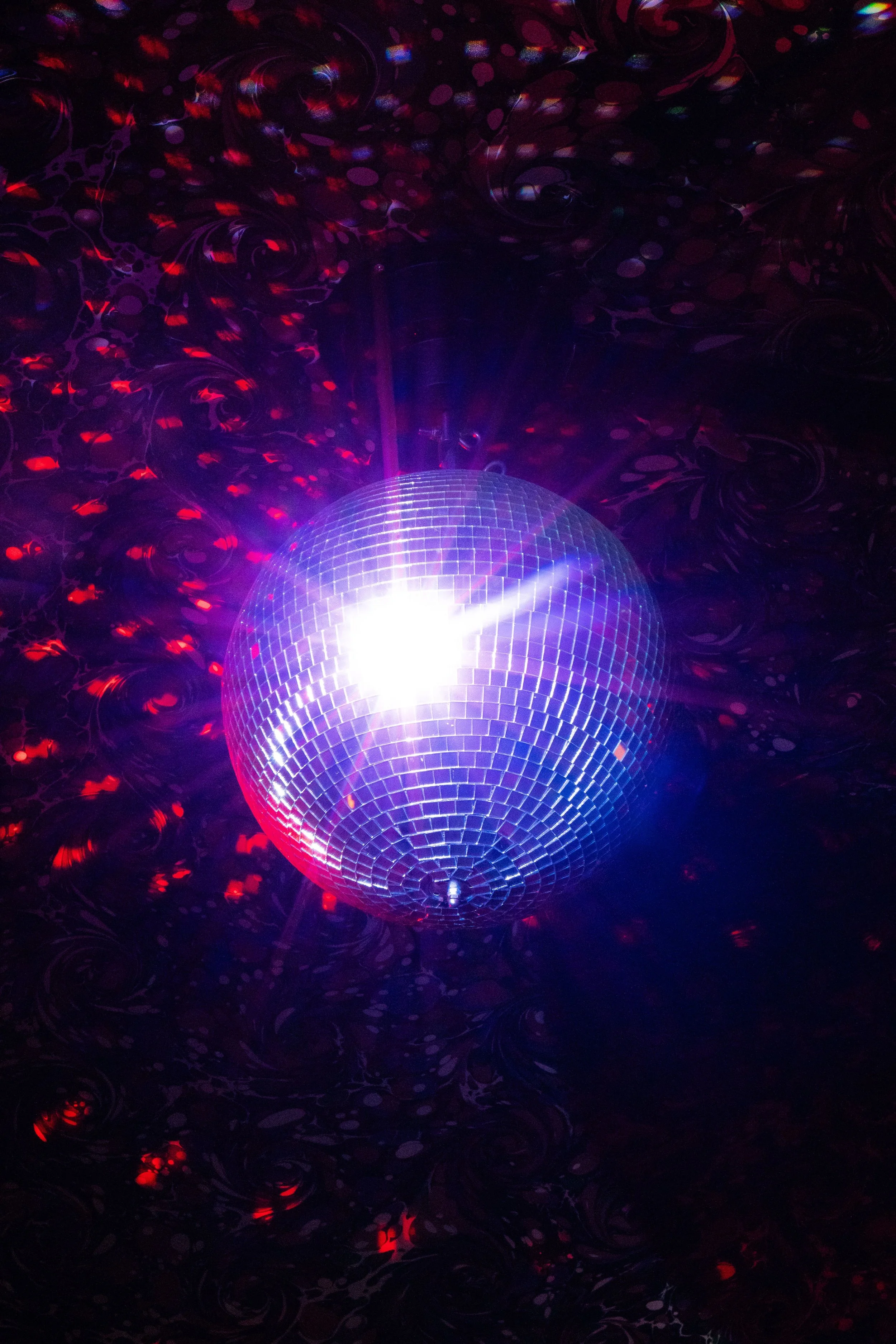 A large disco ball emitting purple and white light against a dark background with swirling red and purple patterns.
