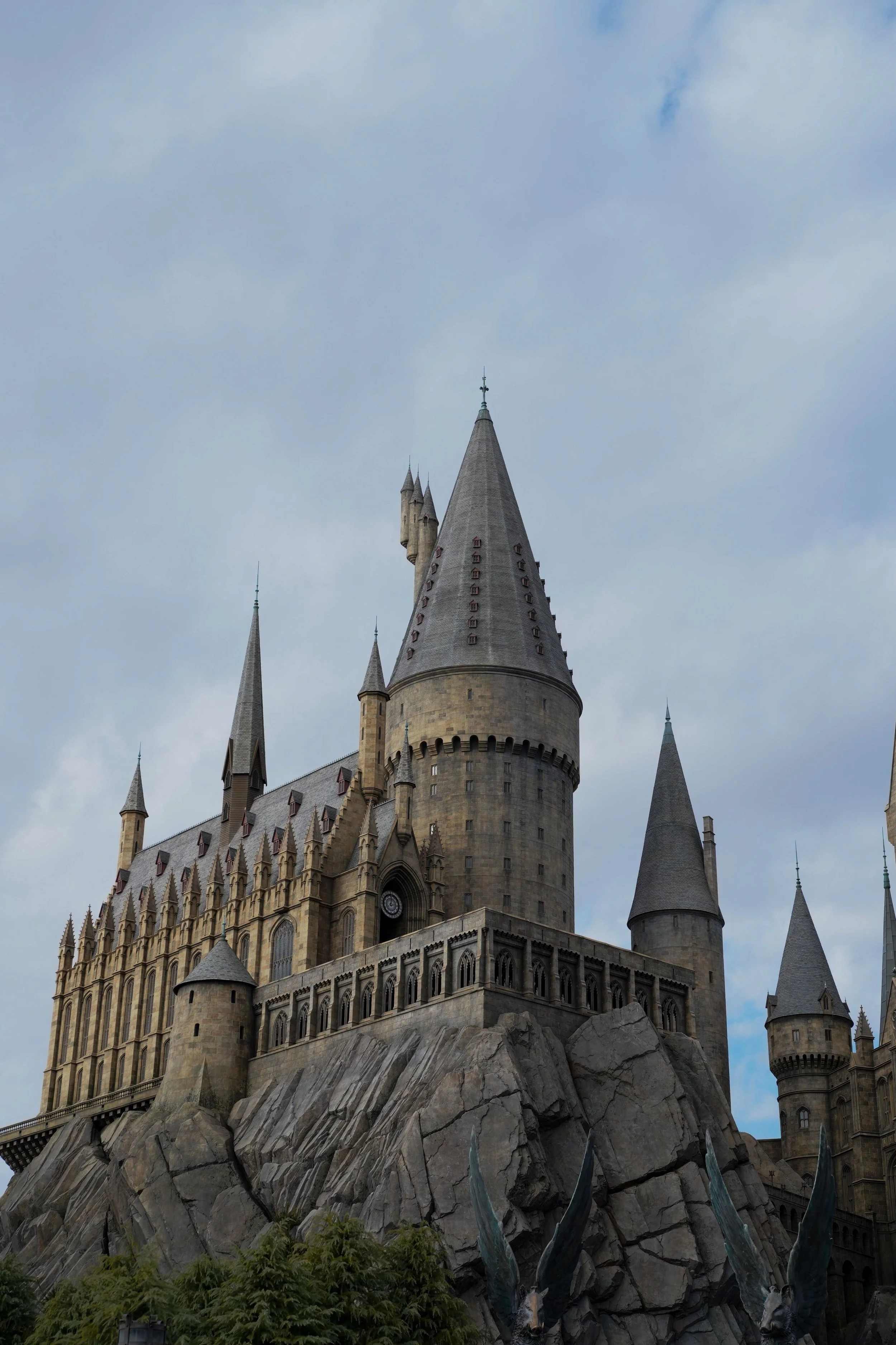 A castle with multiple pointed towers and a rocky base under a cloudy sky.