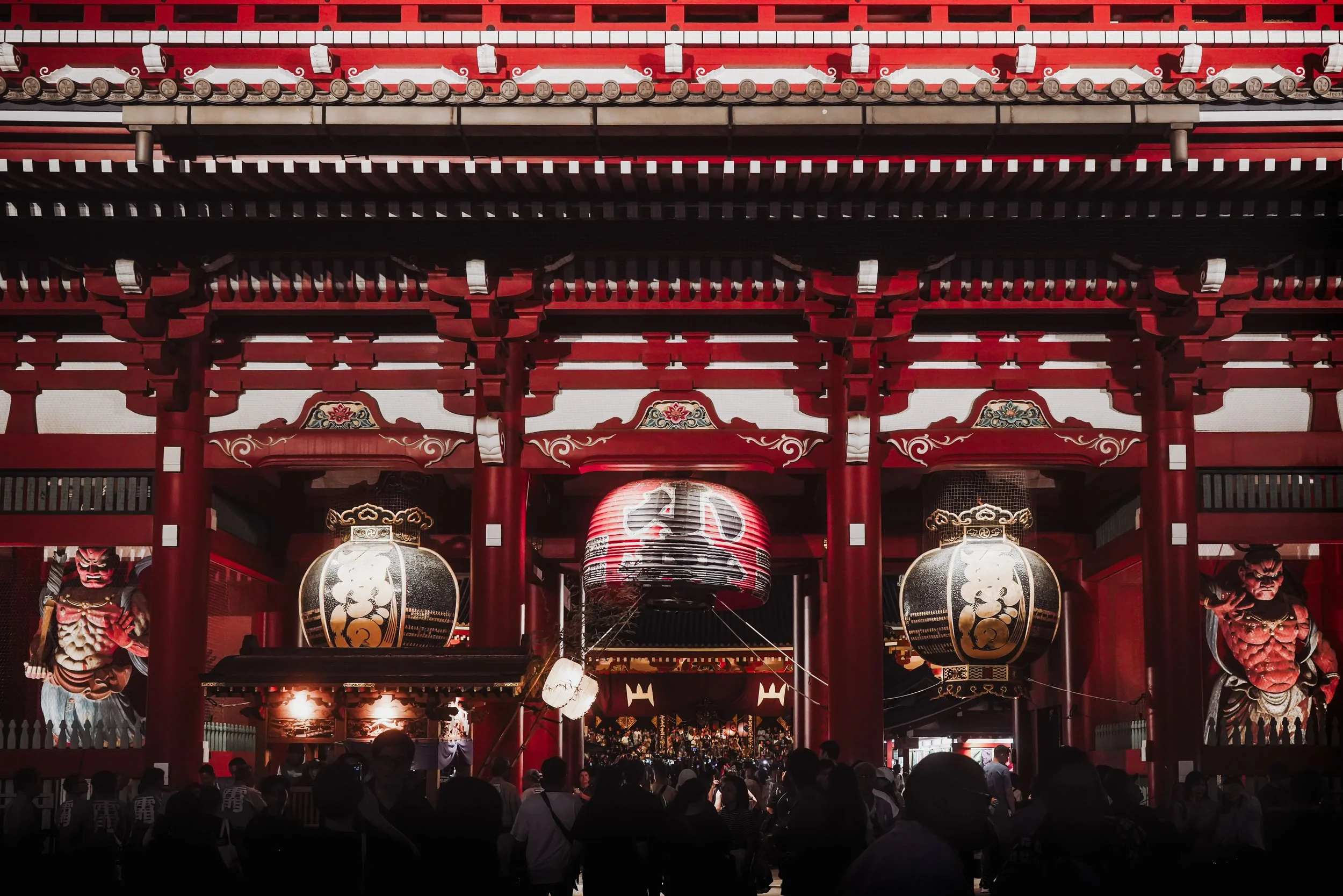 A busy downtown street scene in the evening, illuminated by colorful neon signs in Japanese, with a crowd of pedestrians crossing the street and buildings adorned with advertisements and digital billboards.