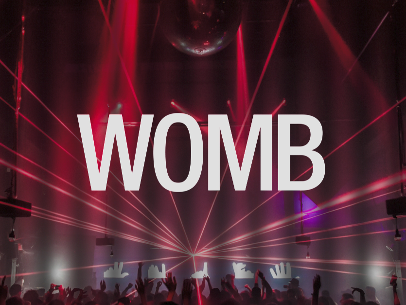Crowd at a concert with laser lights and large screen displaying the word 'WOMB' in bold white letters.