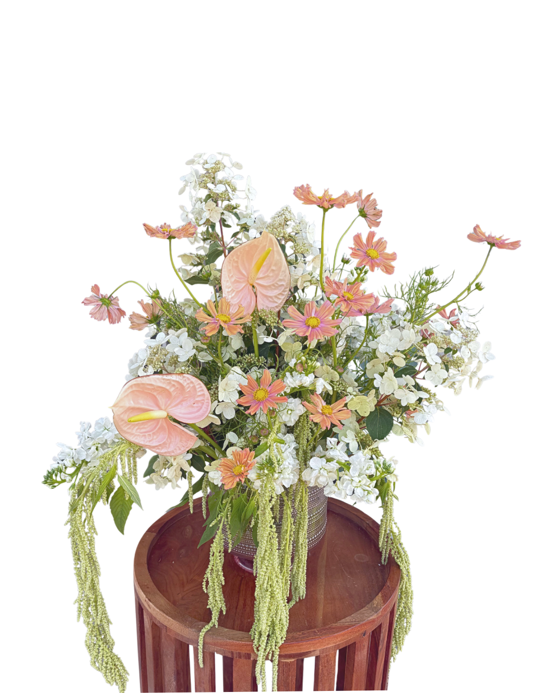 A floral arrangement with pink anthuriums, white hydrangeas, and small pink daisies in a metal container on a wooden table.