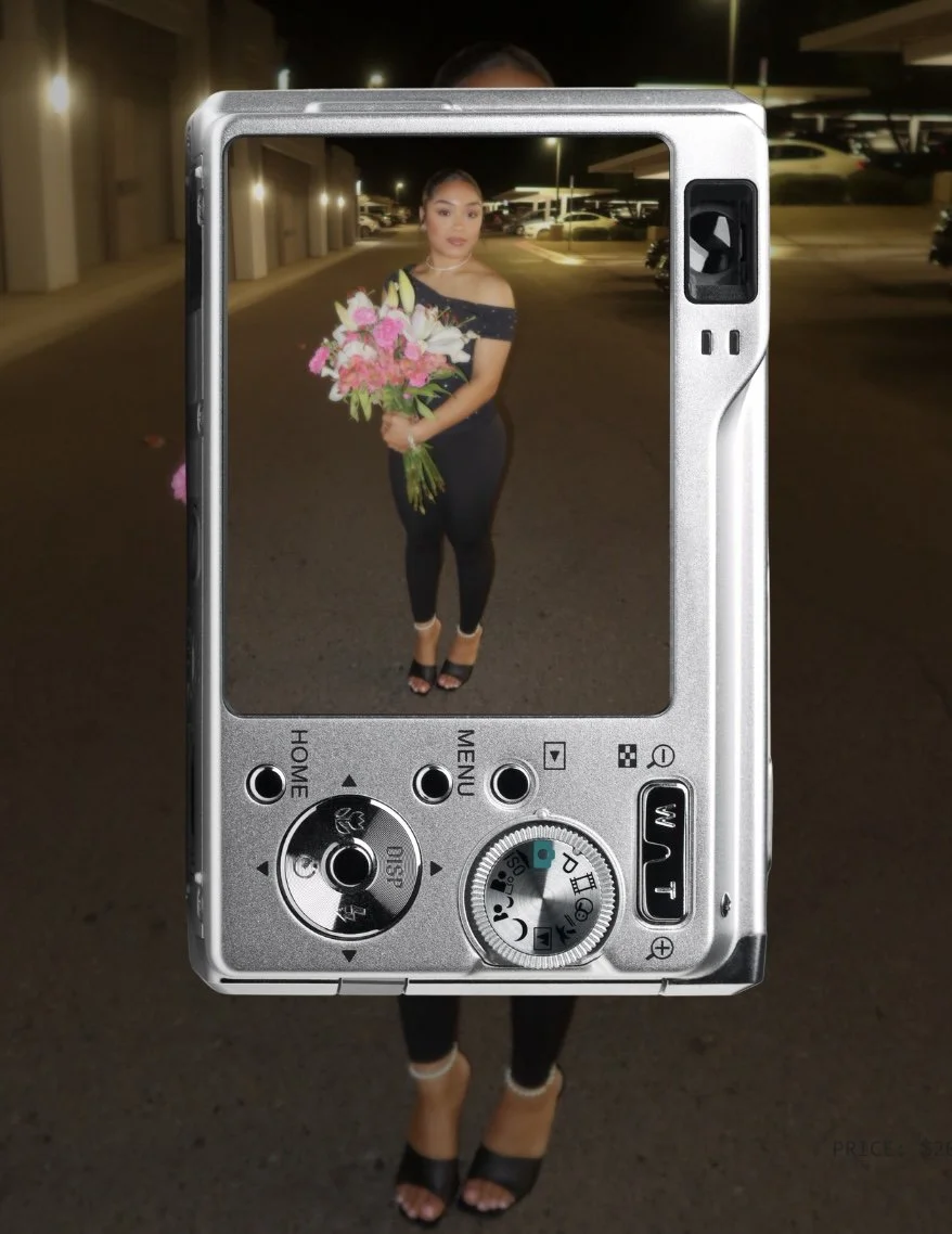 A woman standing in a parking lot at night, holding a bouquet of pink and white flowers, is seen through the LCD screen of a digital camera.