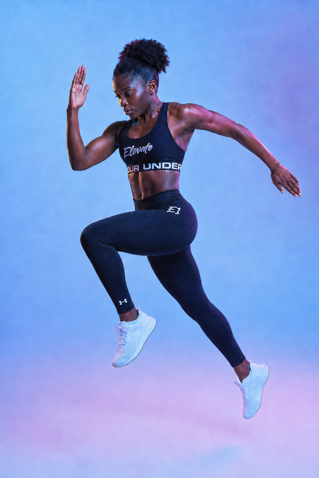 An athletic woman with curly hair tied back is jumping in mid-air against a blue and purple gradient background. She is wearing a black sports bra with the words 'Elevate' and 'Your Under' visible, black leggings, and white athletic shoes.