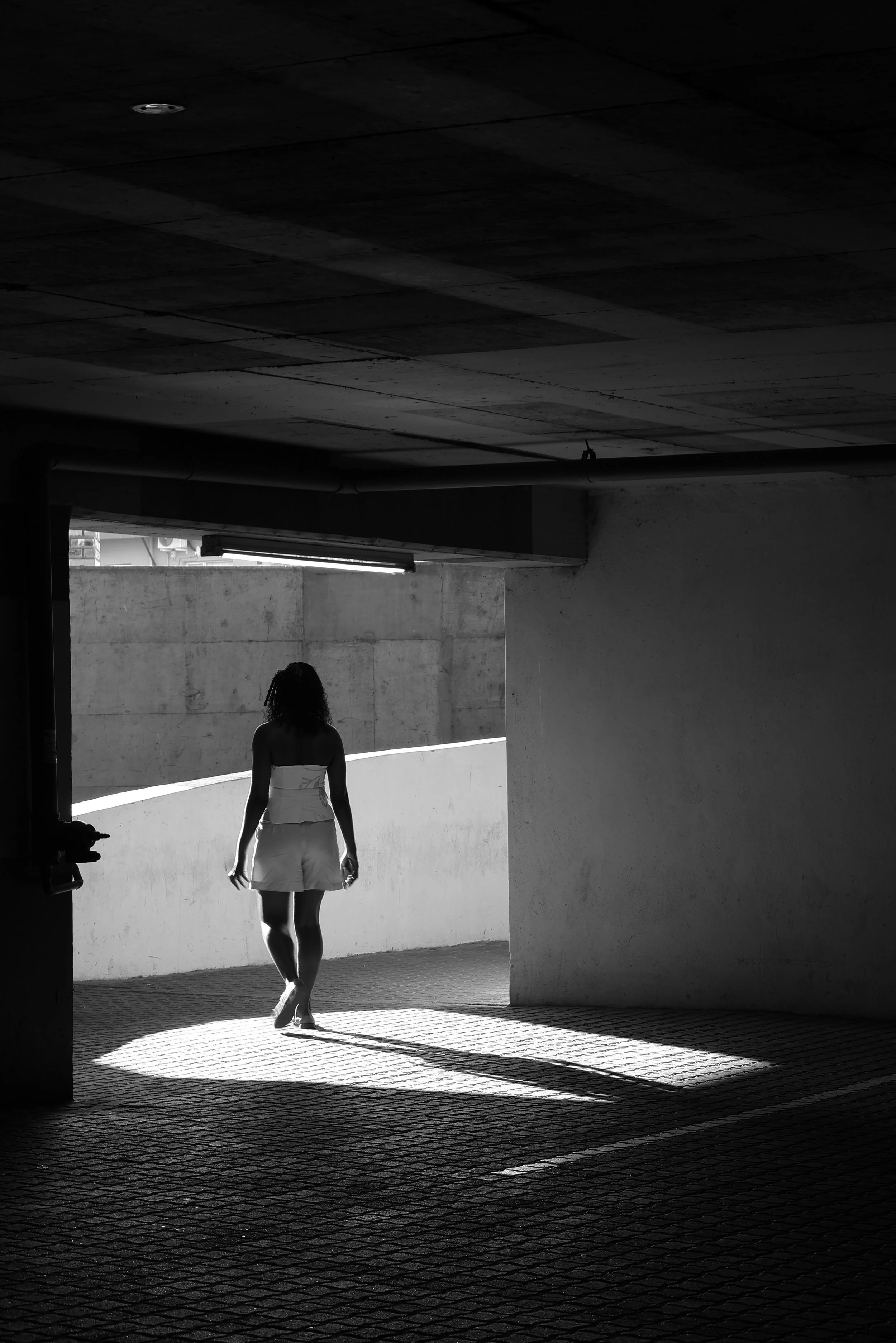 A woman walking in a parking garage with sunlight casting shadows on the ground.