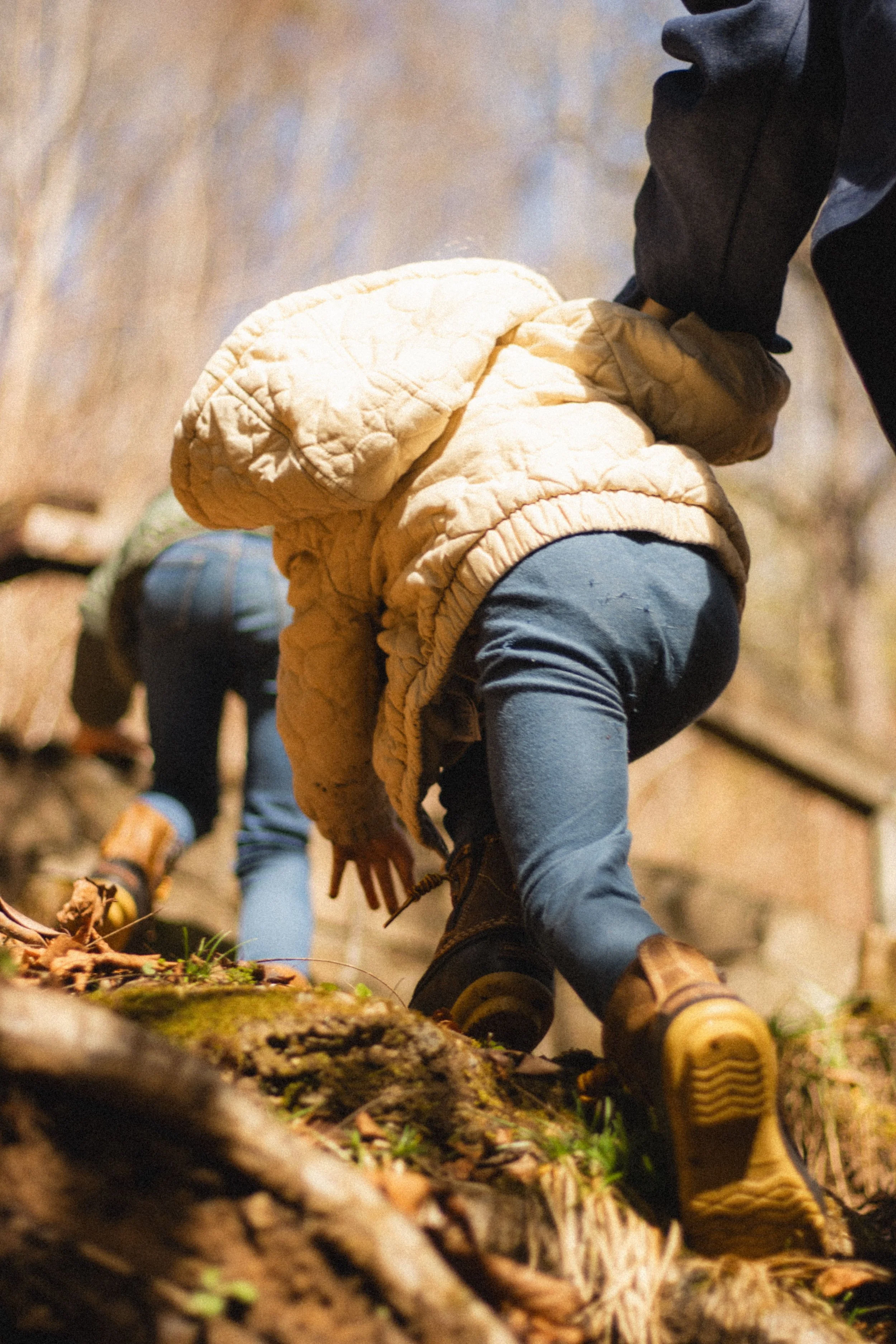People climbing a rocky outdoor trail, with one person in the foreground wearing tan boots and blue jeans, and others in the background, all dressed for hiking or outdoor activity.