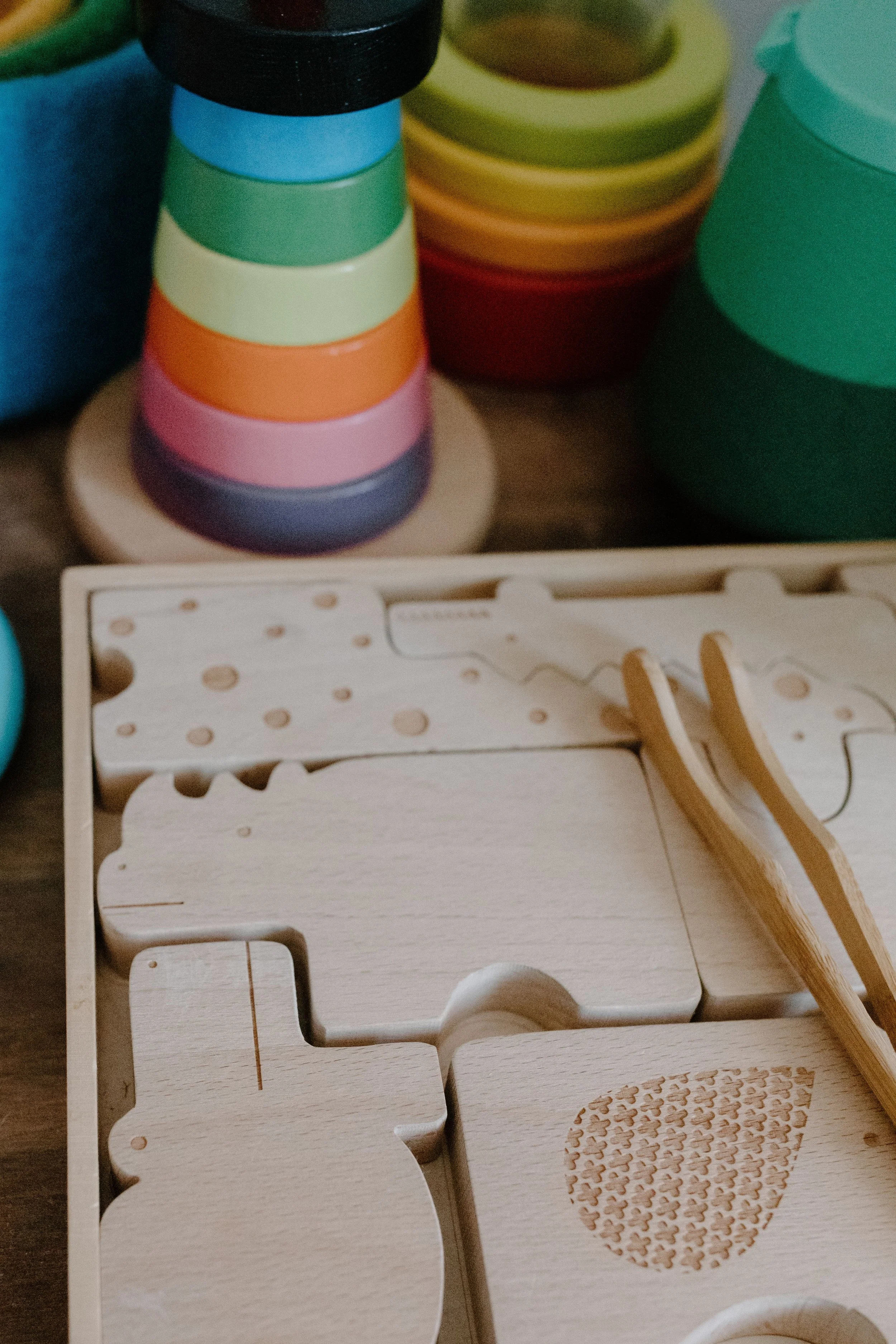 Stacked colorful circular objects, likely cups, and an unfinished wooden craft project with cutout shapes and a pattern, placed on a wooden surface.