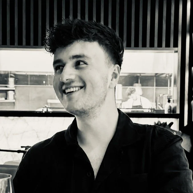 Een blij persoon met kort, gekruld haar in een zwart-shirt, zittend in een restaurant of café, zwart-wit foto.