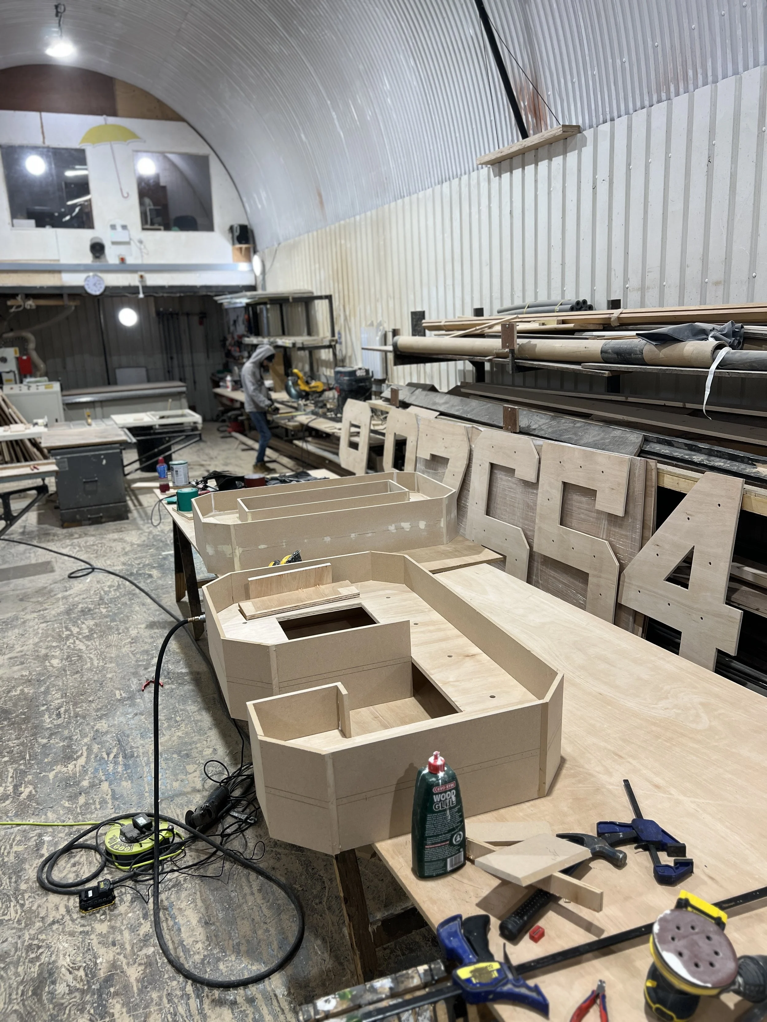 Workshop with woodworking projects in progress, featuring unfinished wooden structures, tools, and equipment.