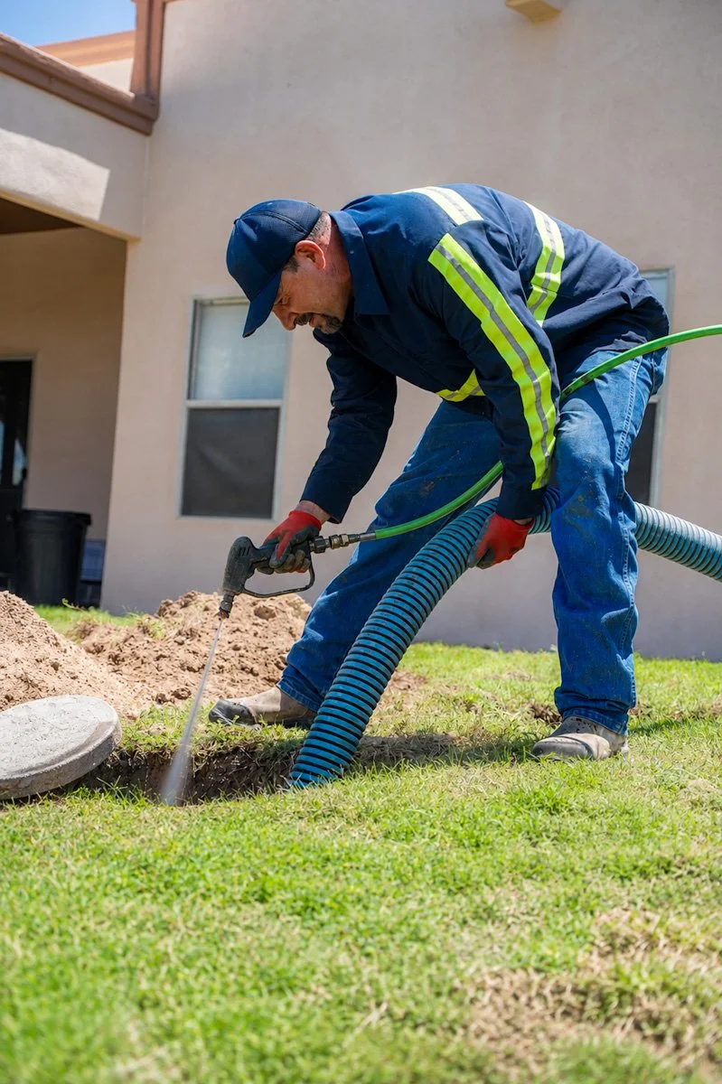 A man in work clothes performing a septic tank pumping and cleaning job.