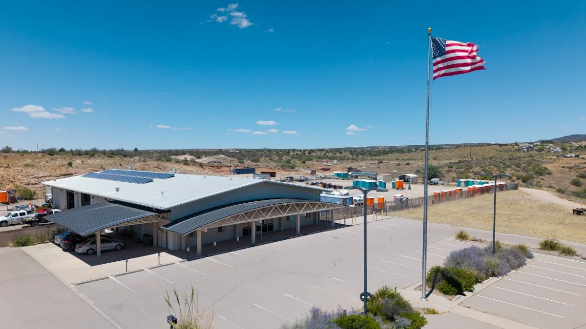 A parking lot with a building, an American flag, and a rural landscape with a blue sky.