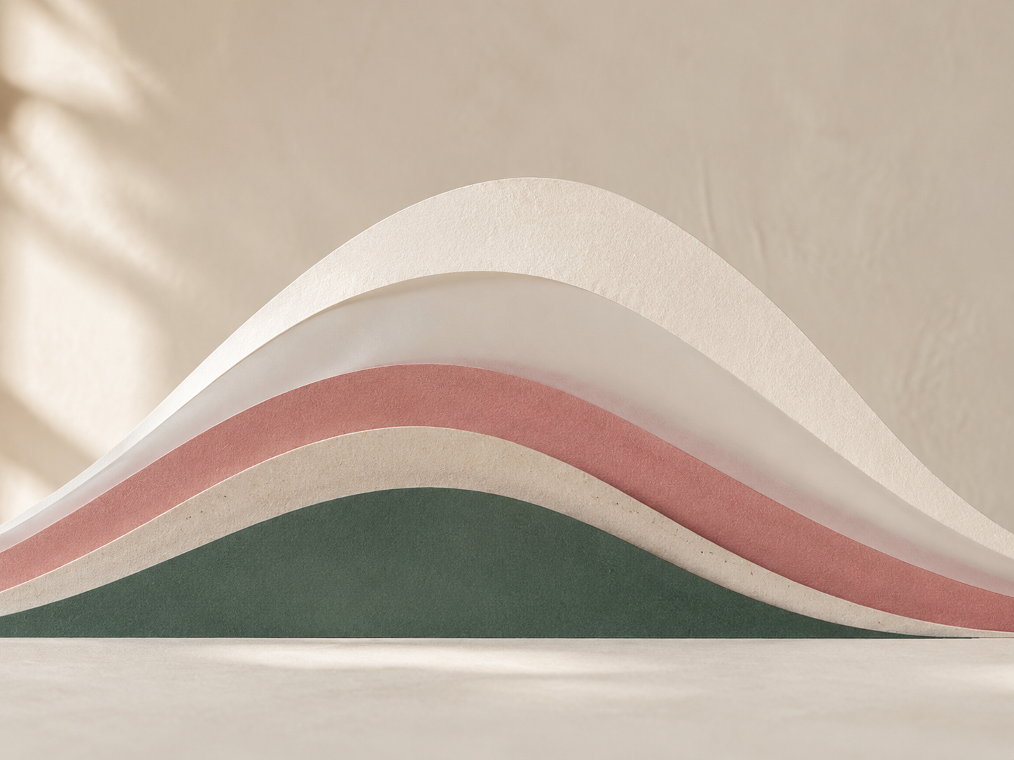 Close-up of layered paper sheets in beige, white, pink, and green colors, curling upward against a blurred beige background.
