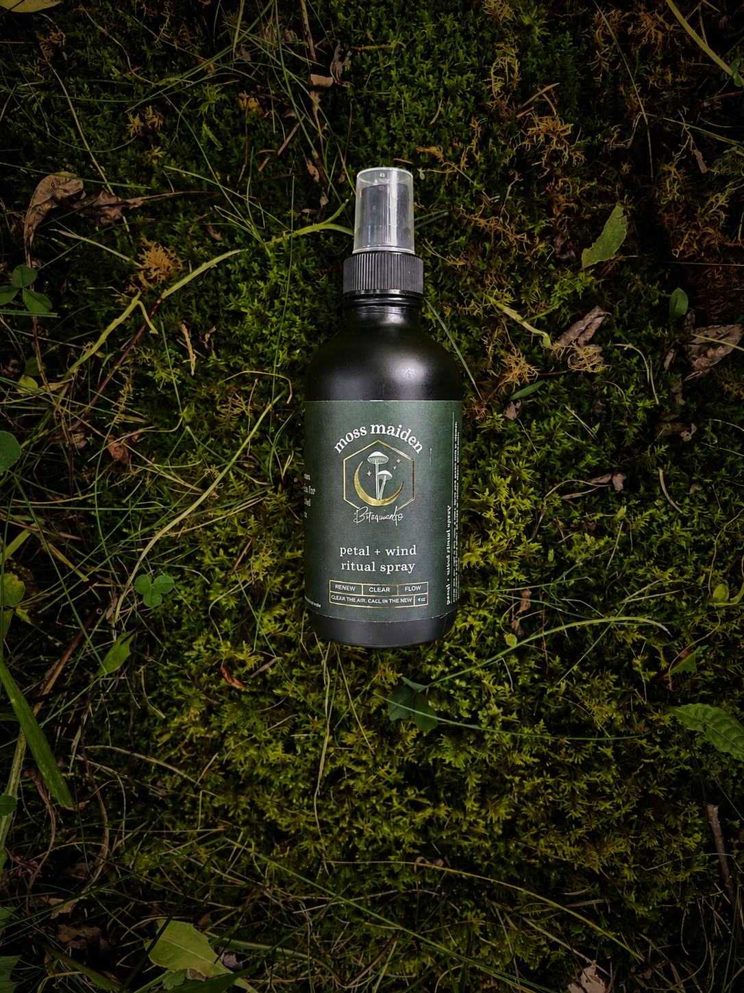 A green bottle of moss maiden petal and wind ritual spray with a spray nozzle, lying on moss and grass