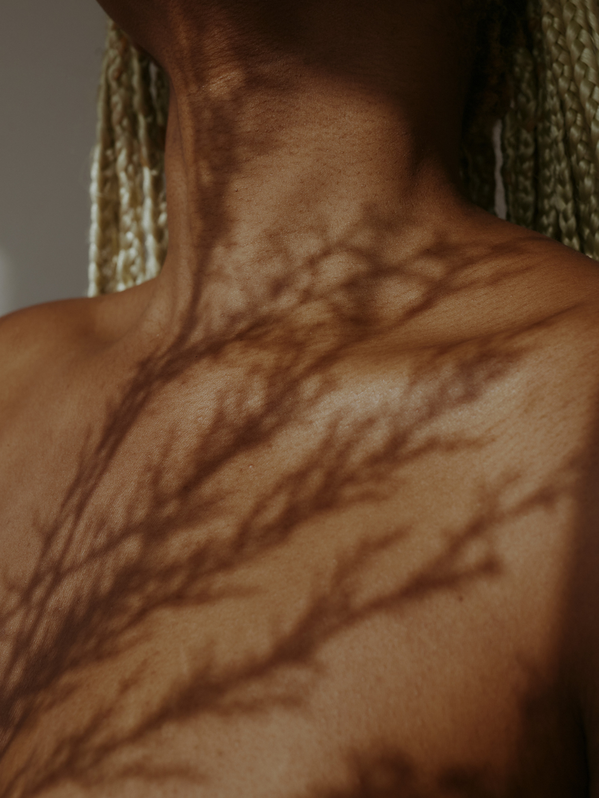 Close-up of a person's neck and shoulder with shadows cast by a plant.