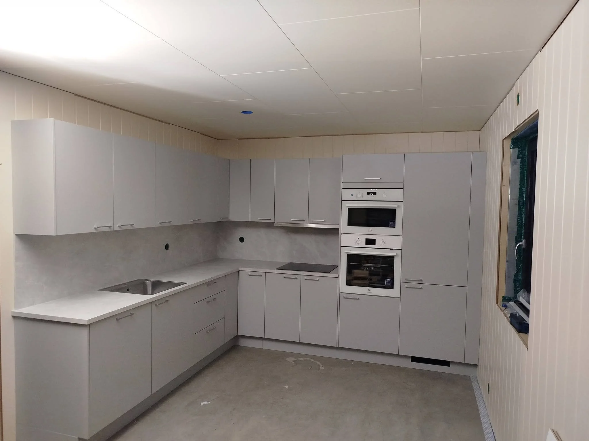 Et moderne kjøkken med hvite skap og integrerte ovner, et komfdelt og vask med stor benkeflate under oppussing.