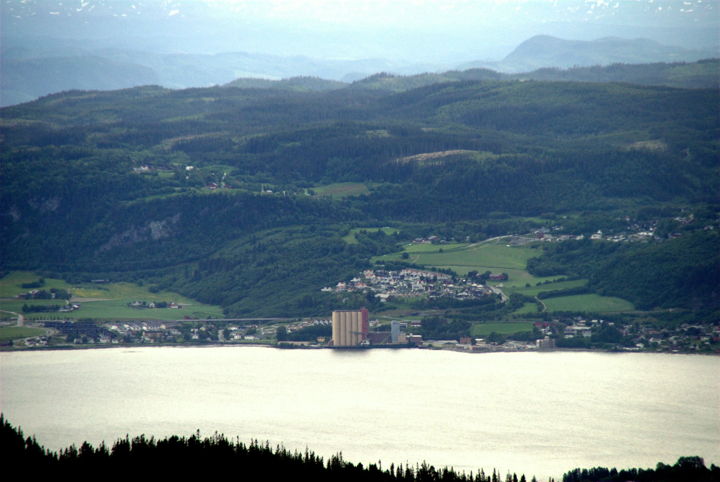 Nærbilde av en innsjø omgitt av grønne åser og fjell, med Buvika i forgrunnen.