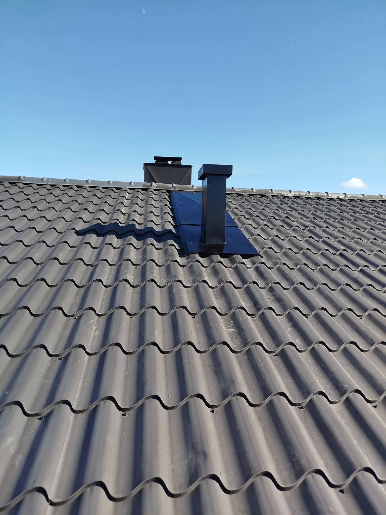 Taket av et hus med betongtakstein og to ventilasjonskonstruksjoner på taket under klar blå himmel.