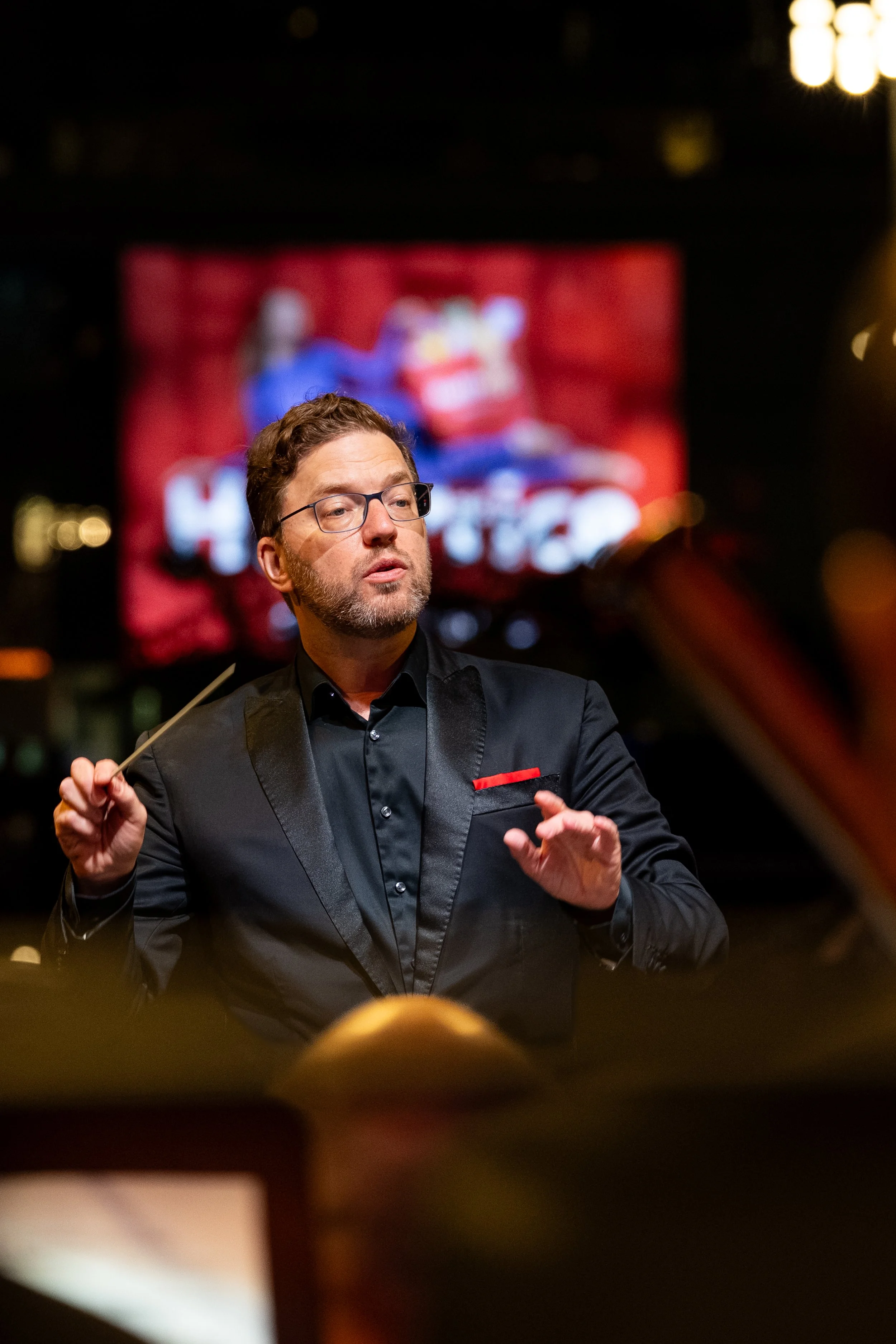 Man in glasses and a black suit speaking onstage in front of a colorful screen