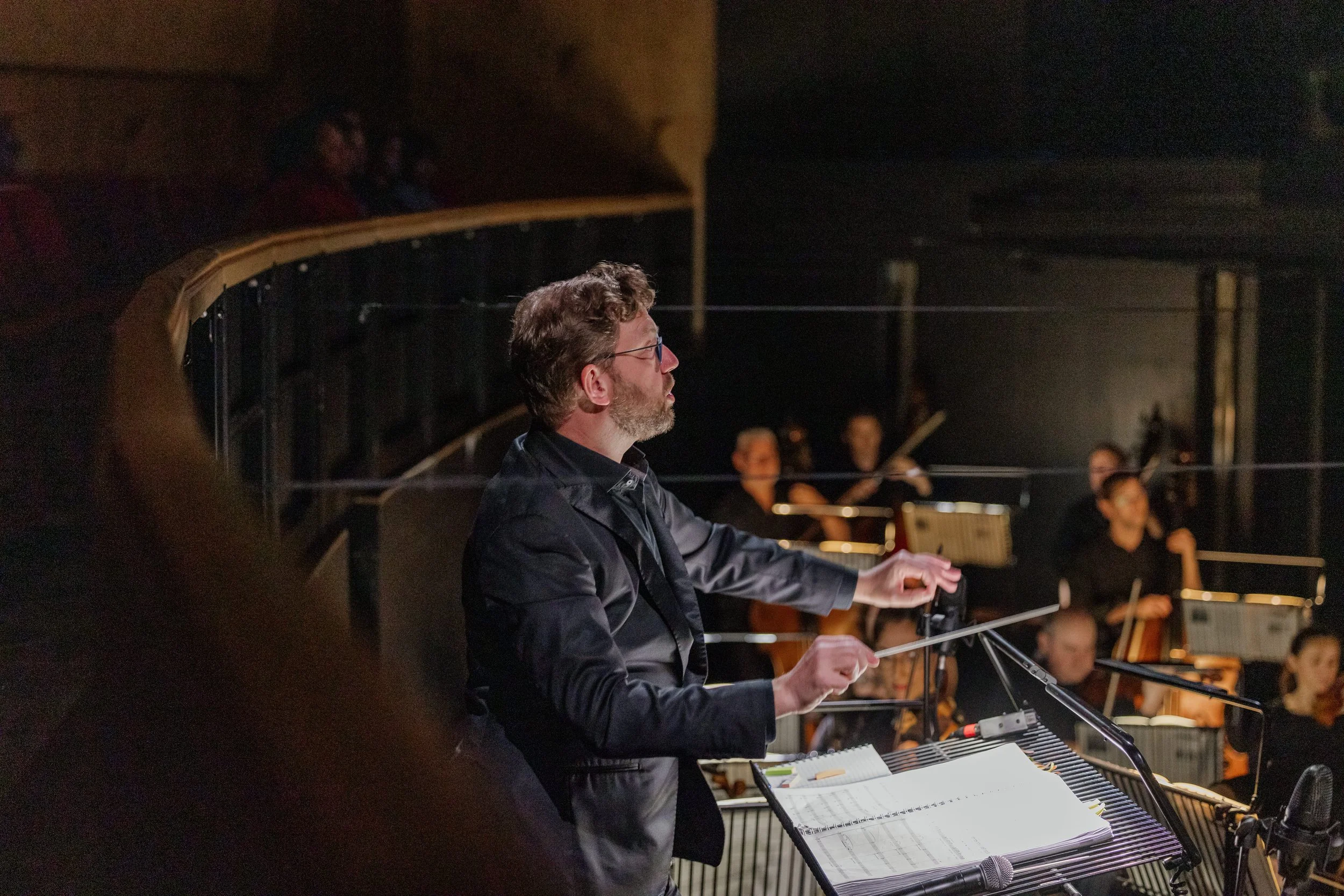 Conductor directing an orchestra during a live performance with sheet music on a music stand