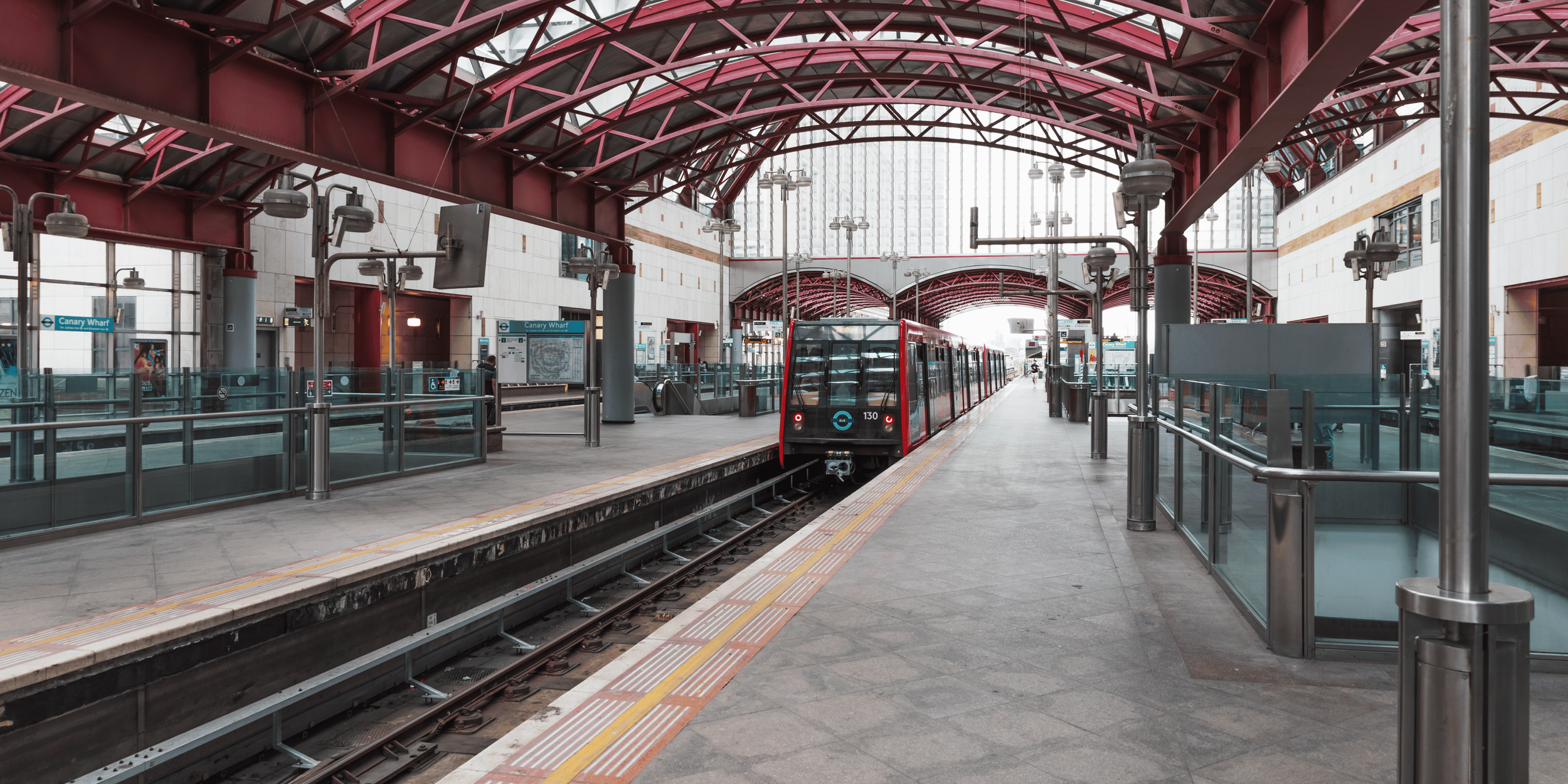 An underground train station with a red train on the track, modern architecture, and a high, arched ceiling with glass panels.