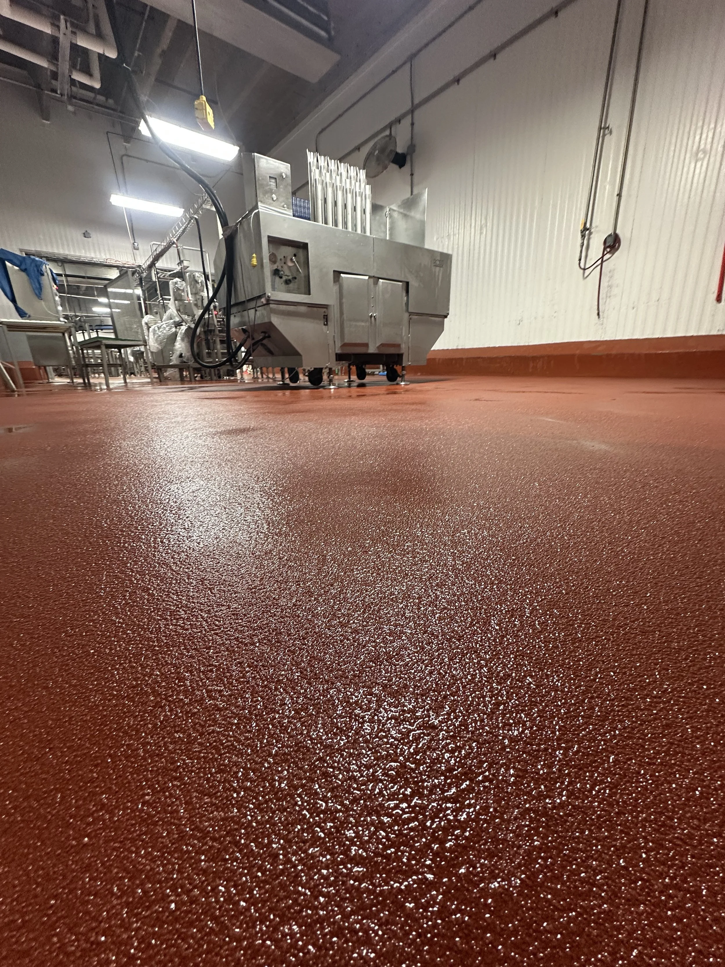 A room with a textured red floor, stainless steel equipment, and a white corrugated wall. There are some bright lights and hanging cords visible.