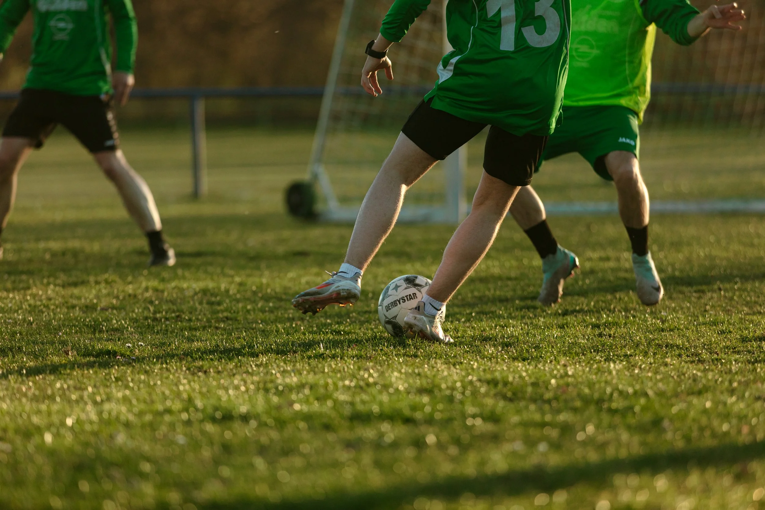 Fußballspieler in grüner Kleidung kicking ball auf Fußballfeld bei Sonnenuntergang.