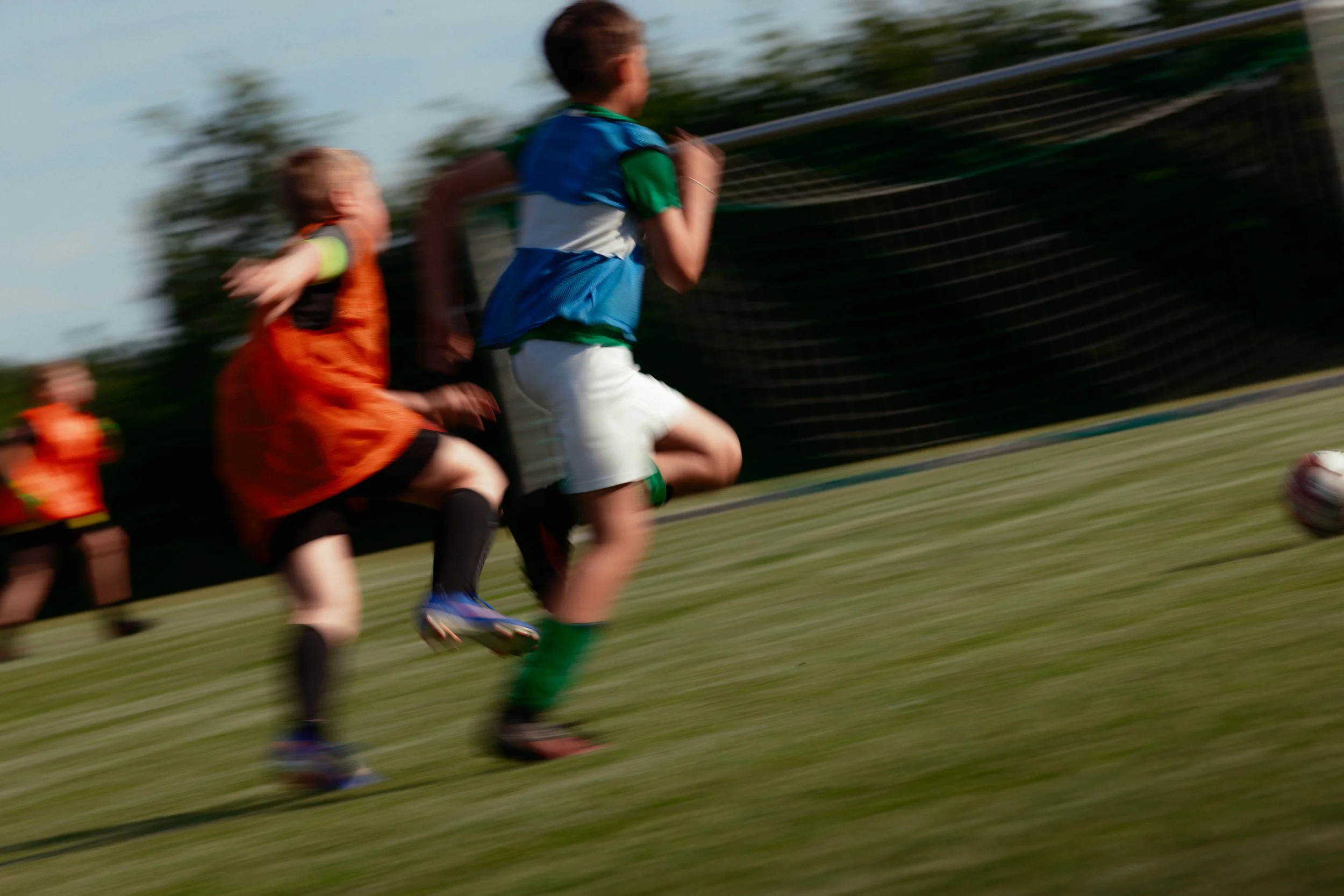 Jugendliche beim Fußballspielen auf einem Sportplatz, Bewegung und Geschwindigkeit sichtbar durch Bewegungsunschärfe.