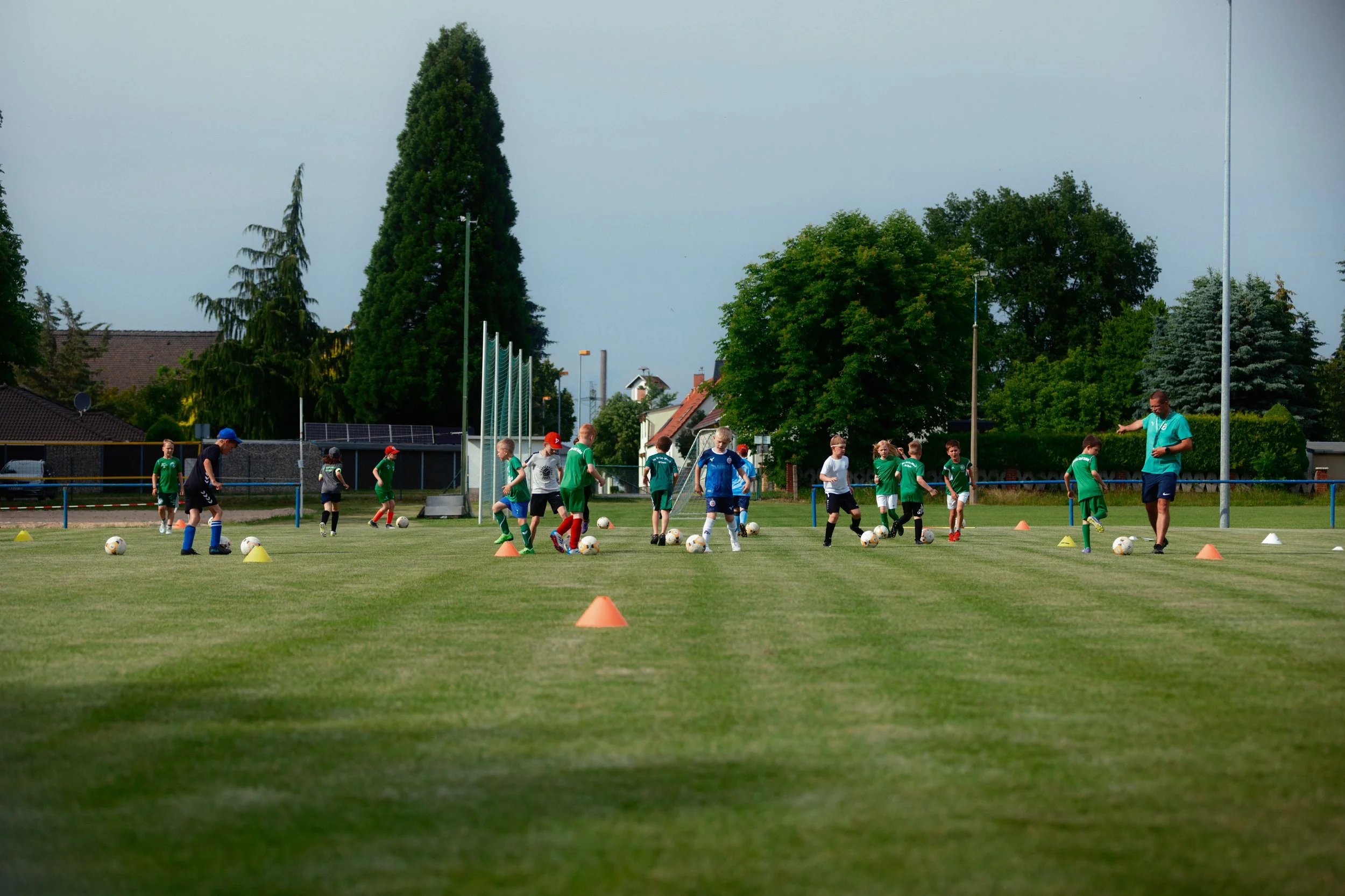 Kinder beim Fußballtraining auf dem Sportfeld, betreut von einem Trainer.