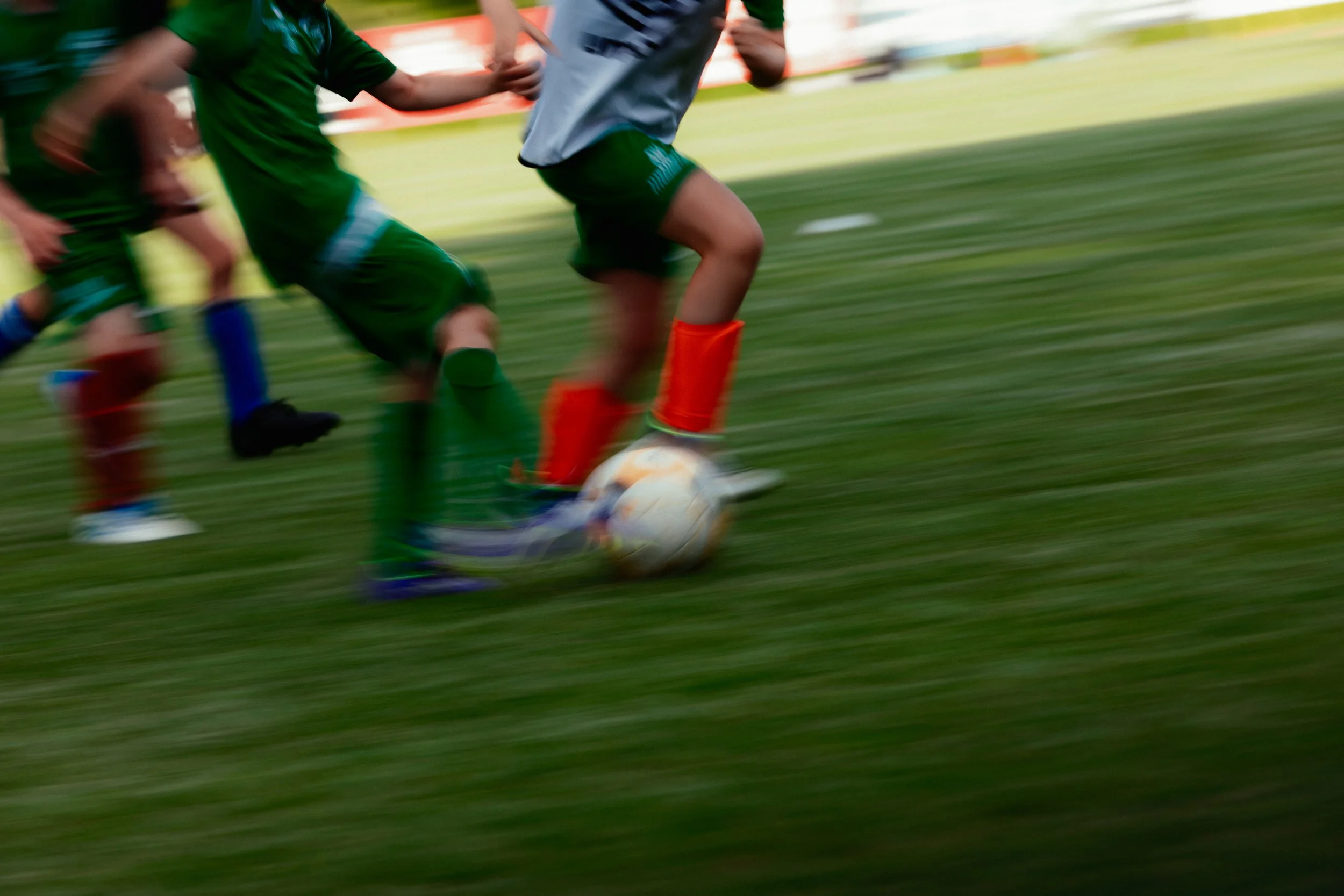 Fußballspiel mit mehreren Spielern, die auf einem grünen Fußballplatz herumlaufen, ein Spieler ist dabei, den Ball mit den Beinen zu kontrollieren.