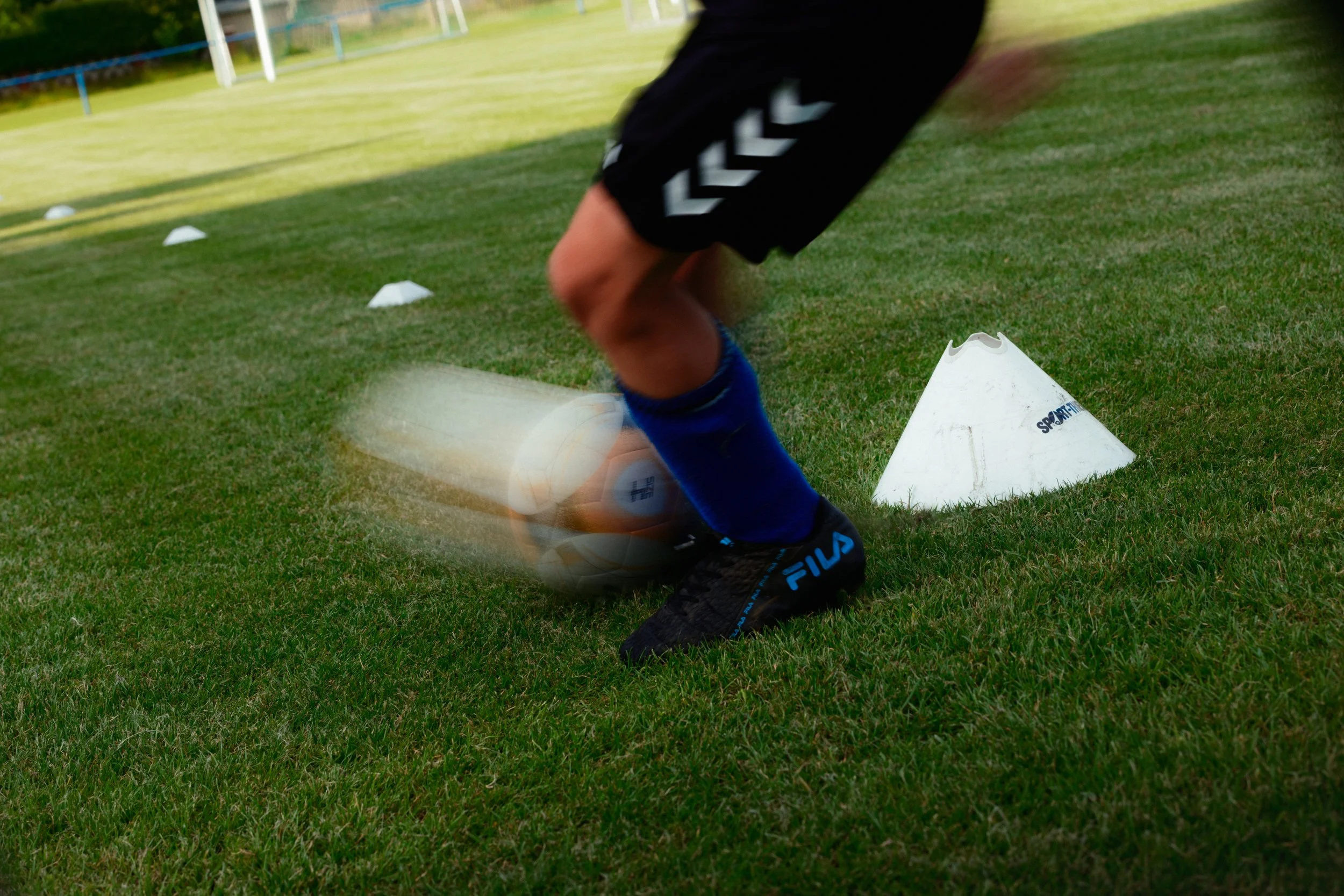 Ein Kind in Sportkleidung rennt auf einem Fußballfeld um eine weiße Markierung, während die Kamera während der Bewegung unscharf ist.
