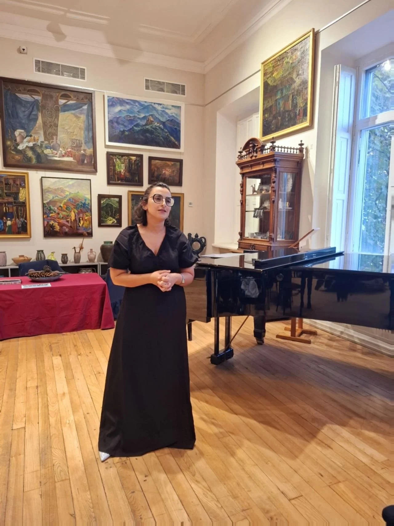 Tinatin Gudadze speaking in a gallery beside a grand piano before a recital