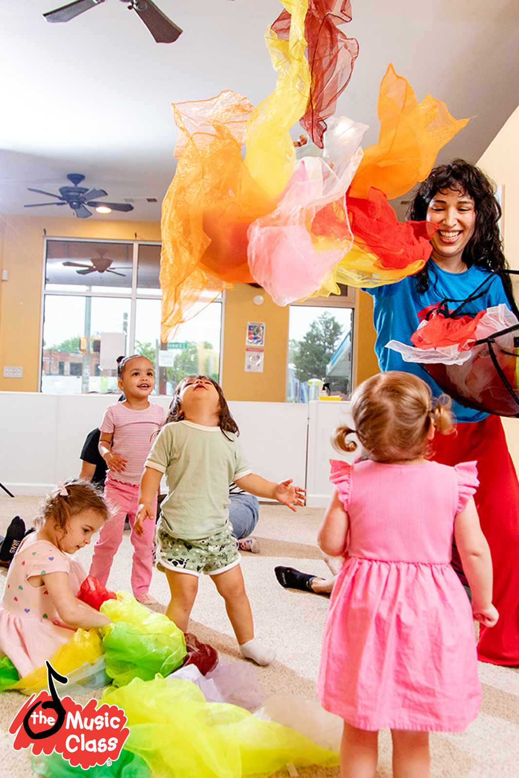 Una maestra y varias niñas en una clase, jugando con tiras de papel de colores, en un ambiente alegre y luminoso.