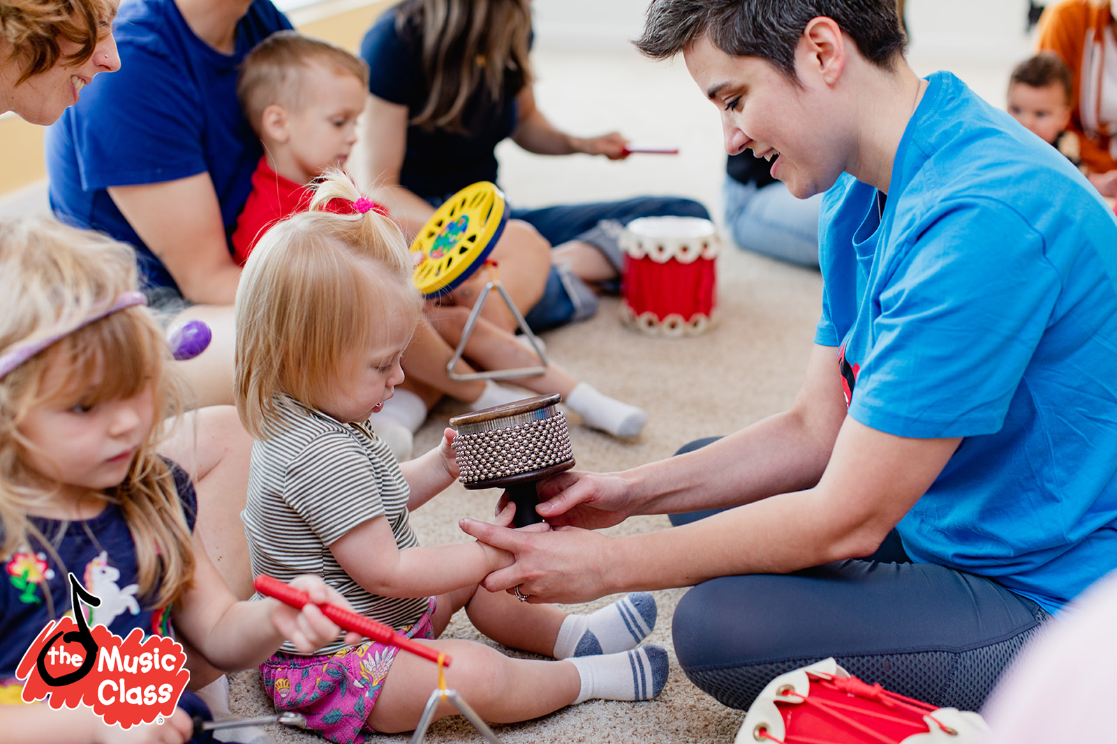 Niños y jóvenes participan en una clase de música en interior, tocando instrumentos como maracas, xilófono y tambor, mientras un instructor los guía, con ambiente alegre y educativo.