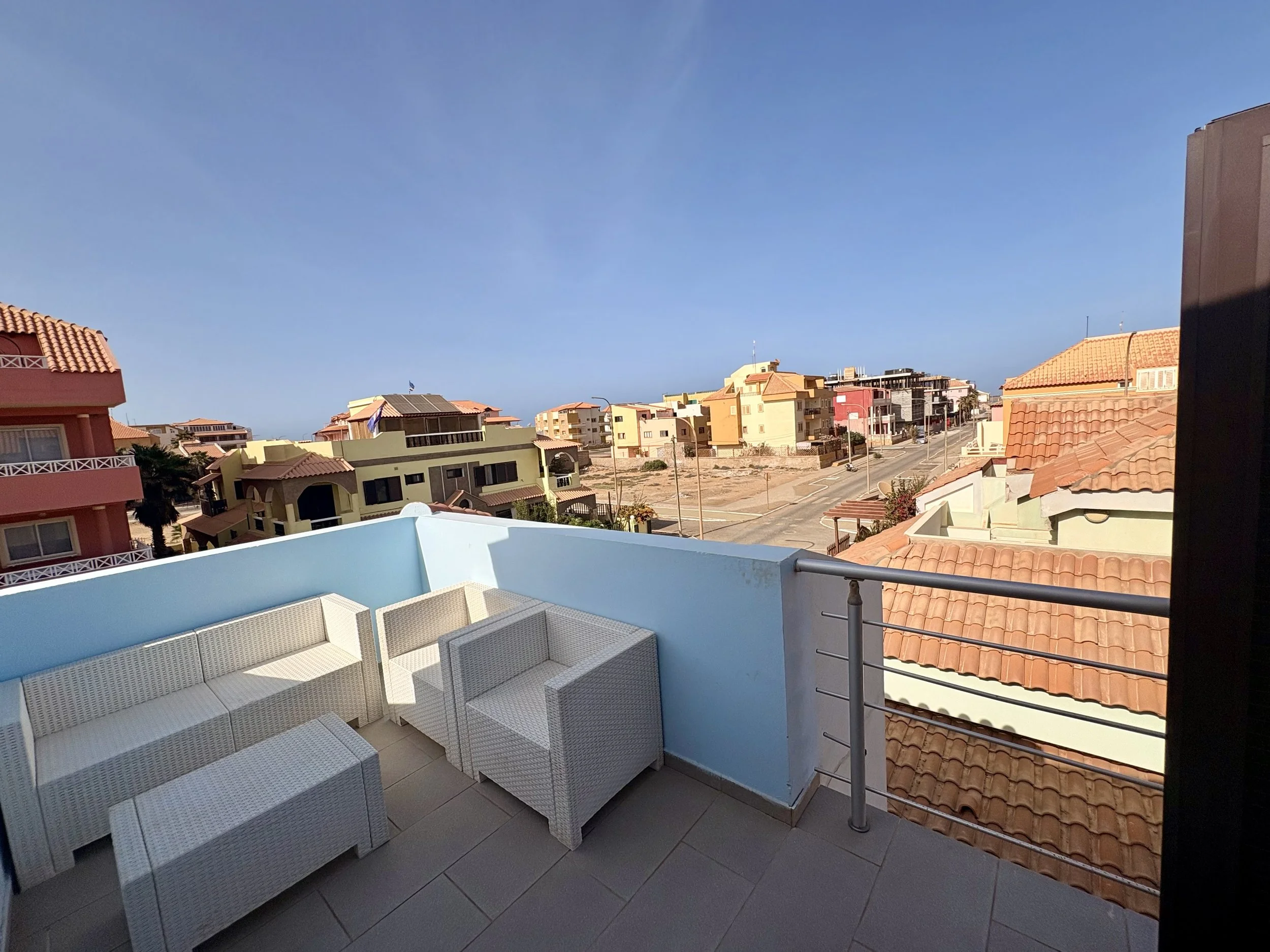 Balcony with outdoor furniture overlooking colorful buildings and a clear blue sky.