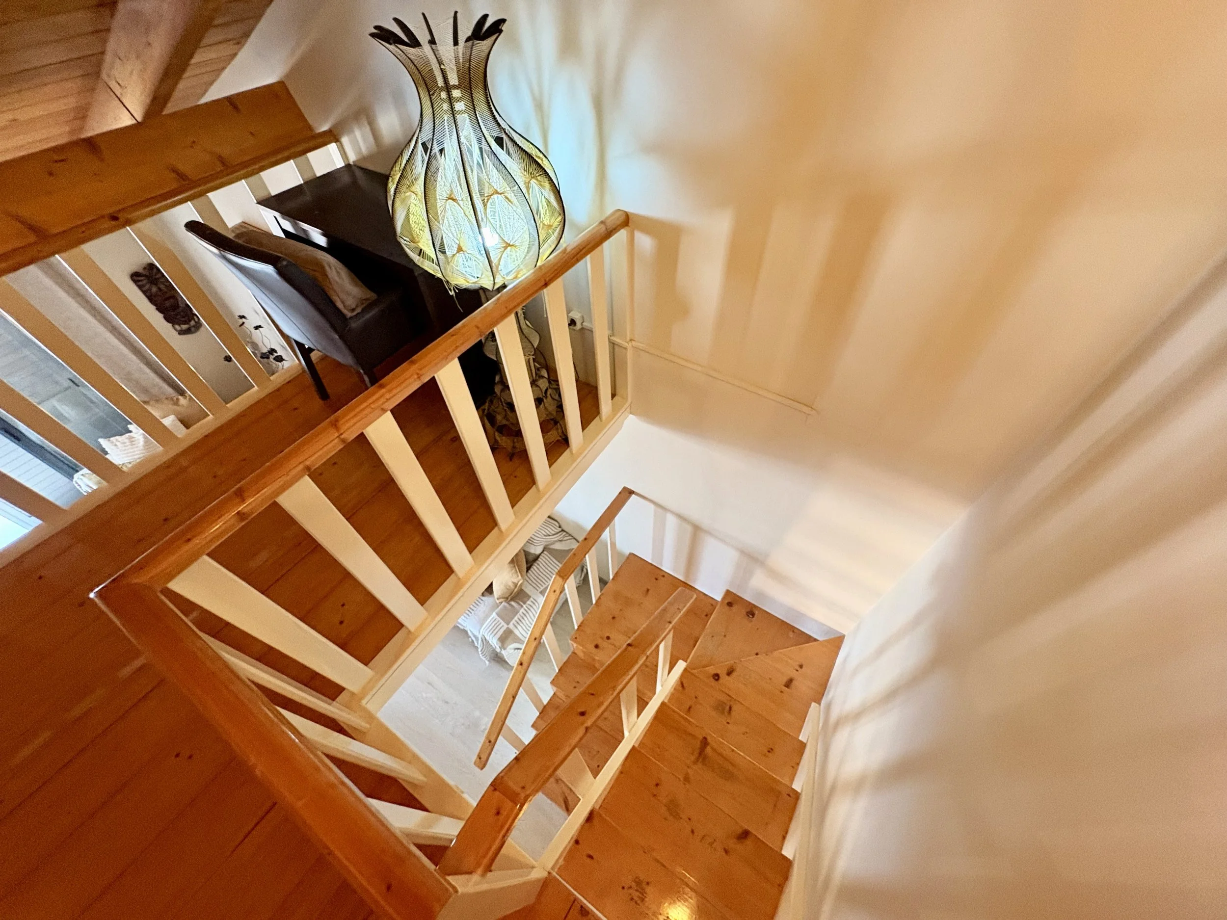 Interior view of a wooden staircase with white railings, leading to an upper floor, with a decorative lampshade on a table in the background.