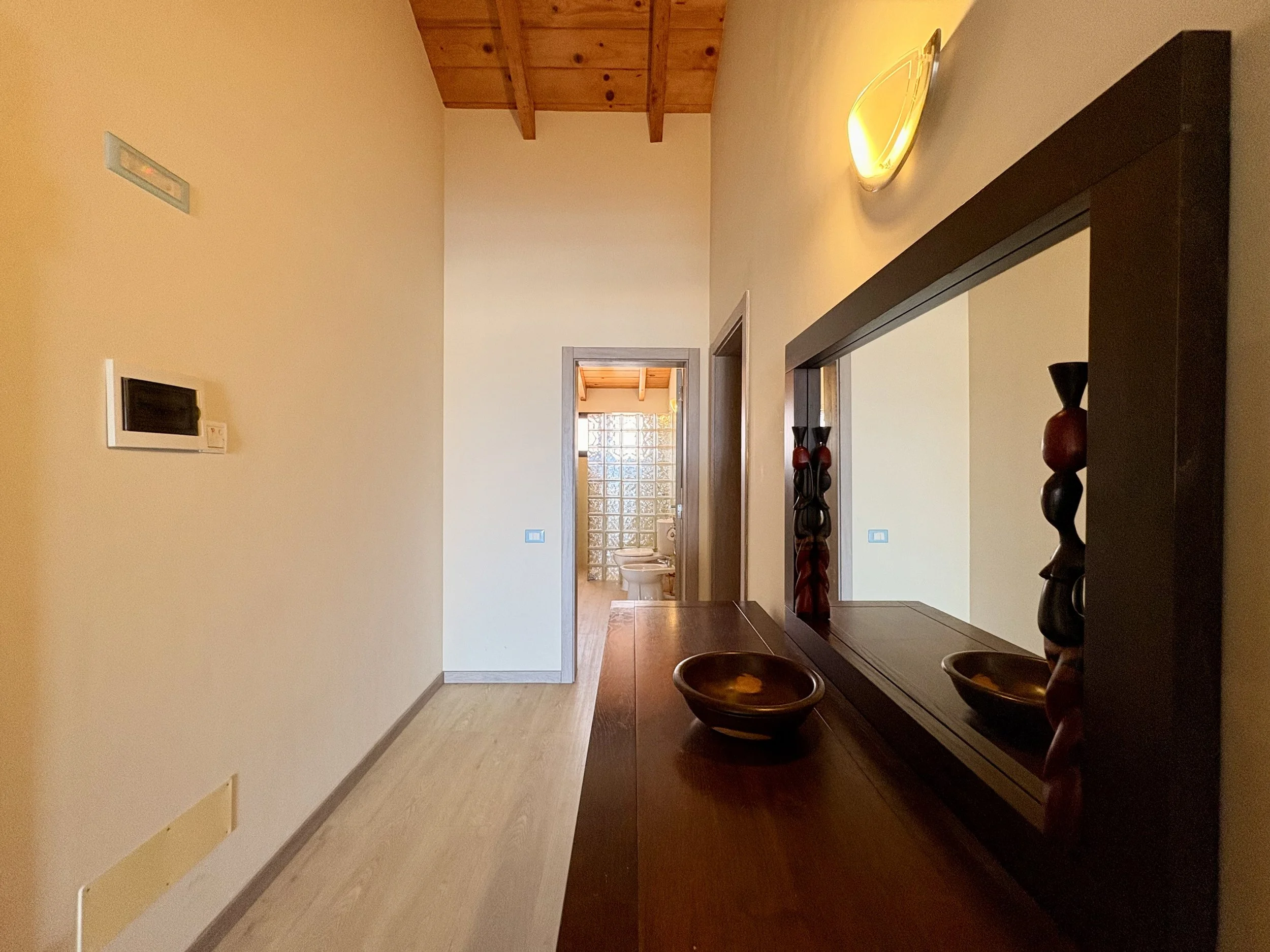 Interior of a home with a hallway, visible bathroom, wooden ceiling, and decorative vases on a dark wooden console.