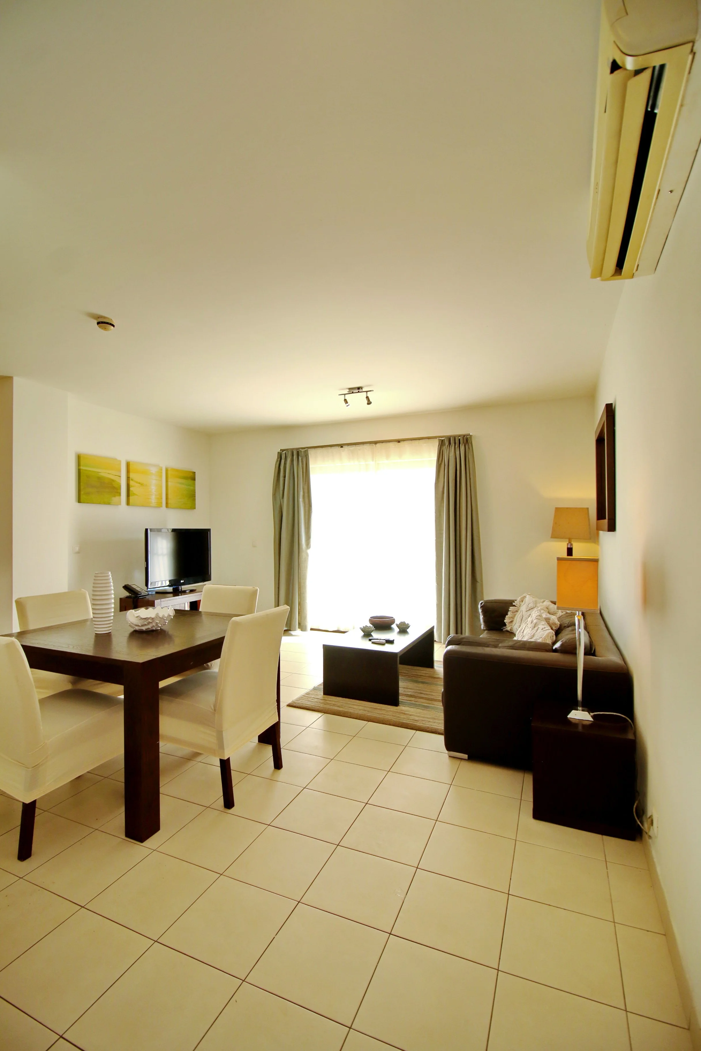 Living room with a tile floor, a dining table with chairs, a sofa, a television, and a window with curtains.