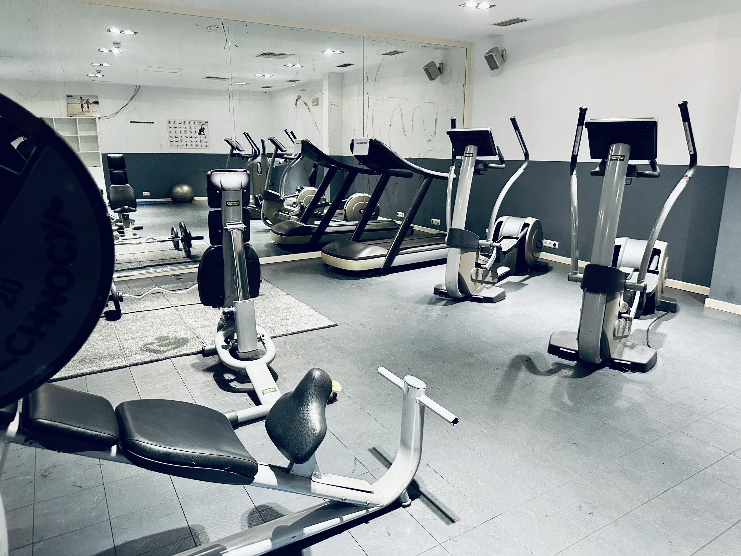 Empty gym room with treadmill and exercise equipment, mirror wall, and a white wall with a photo.