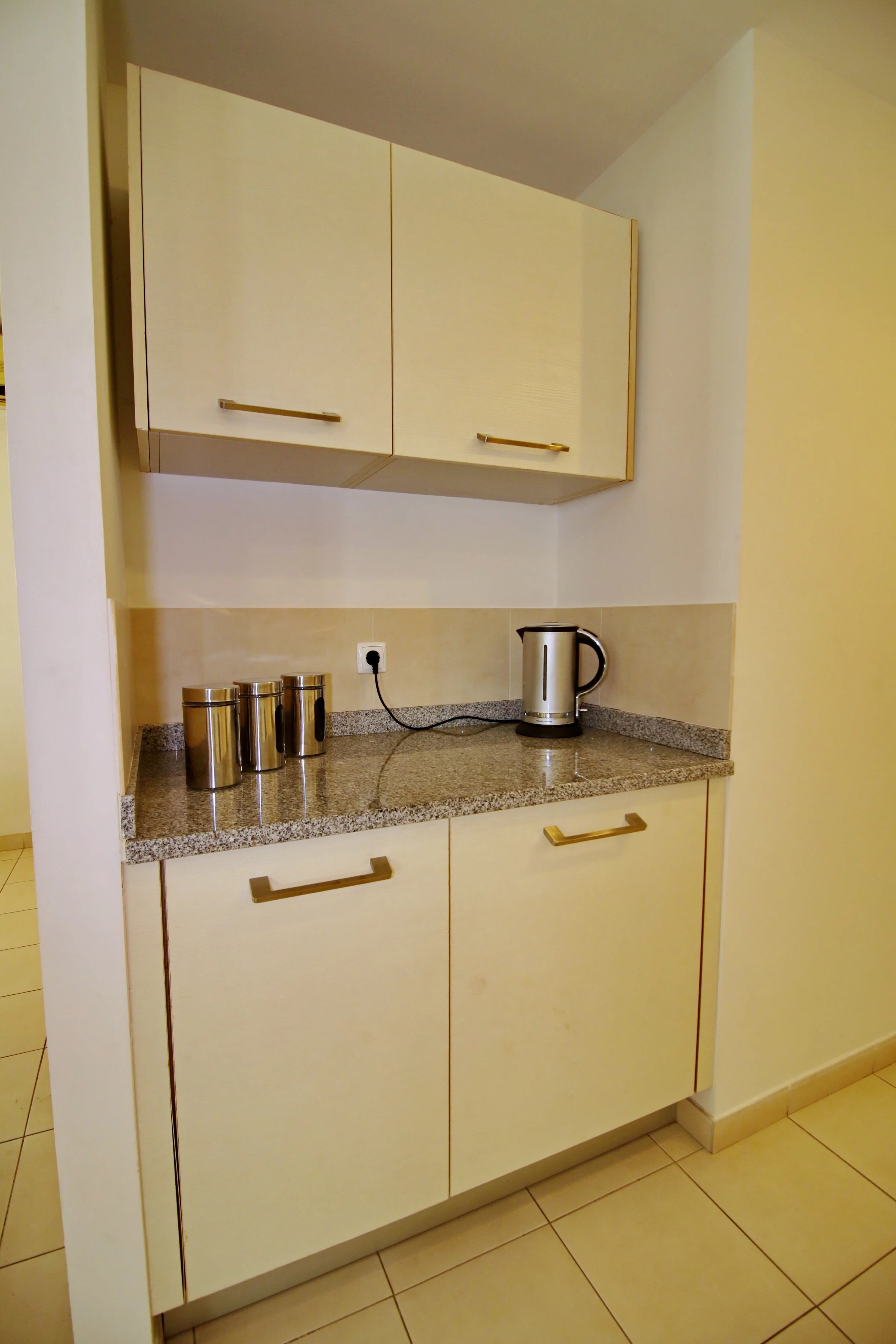 A kitchen counter with three stainless steel canisters, an electric kettle, and an electrical outlet on the wall.