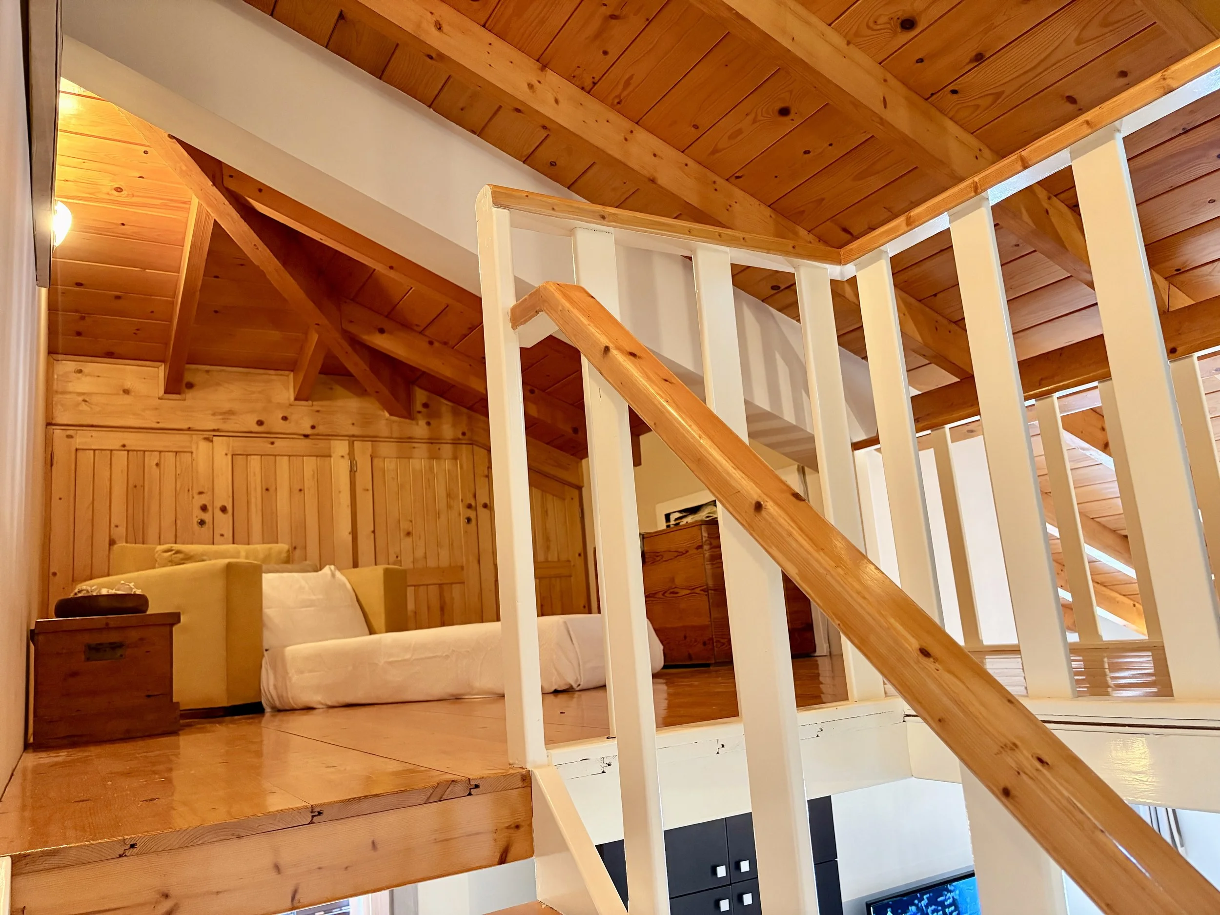 Interior of a cozy wooden cabin bedroom with a white sofa, wooden walls, and a sloped wooden ceiling.
