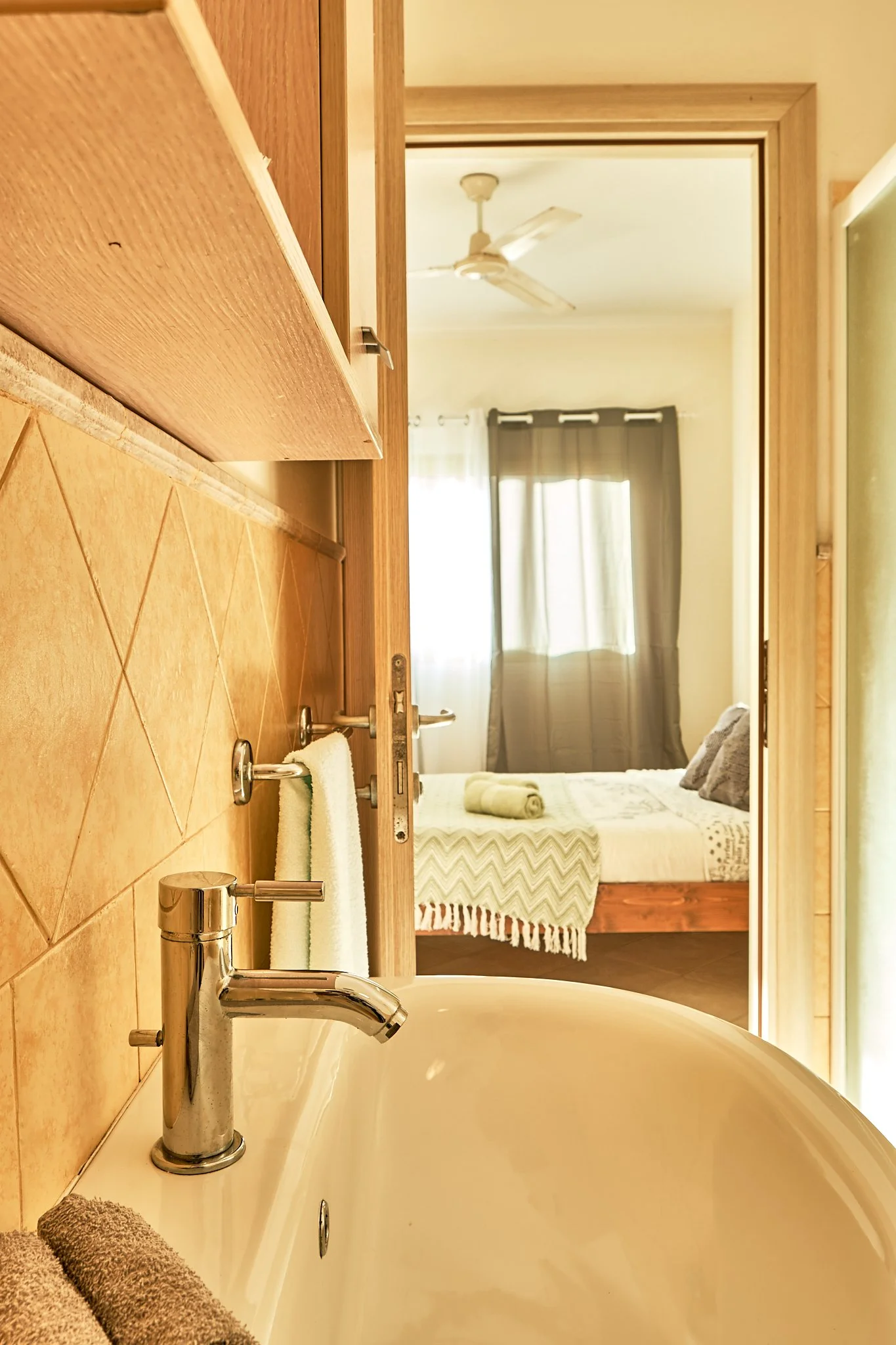 View of a bathroom with a bathtub showing a soap dispenser, towel, and a mirror reflecting a bedroom with a bed and window.