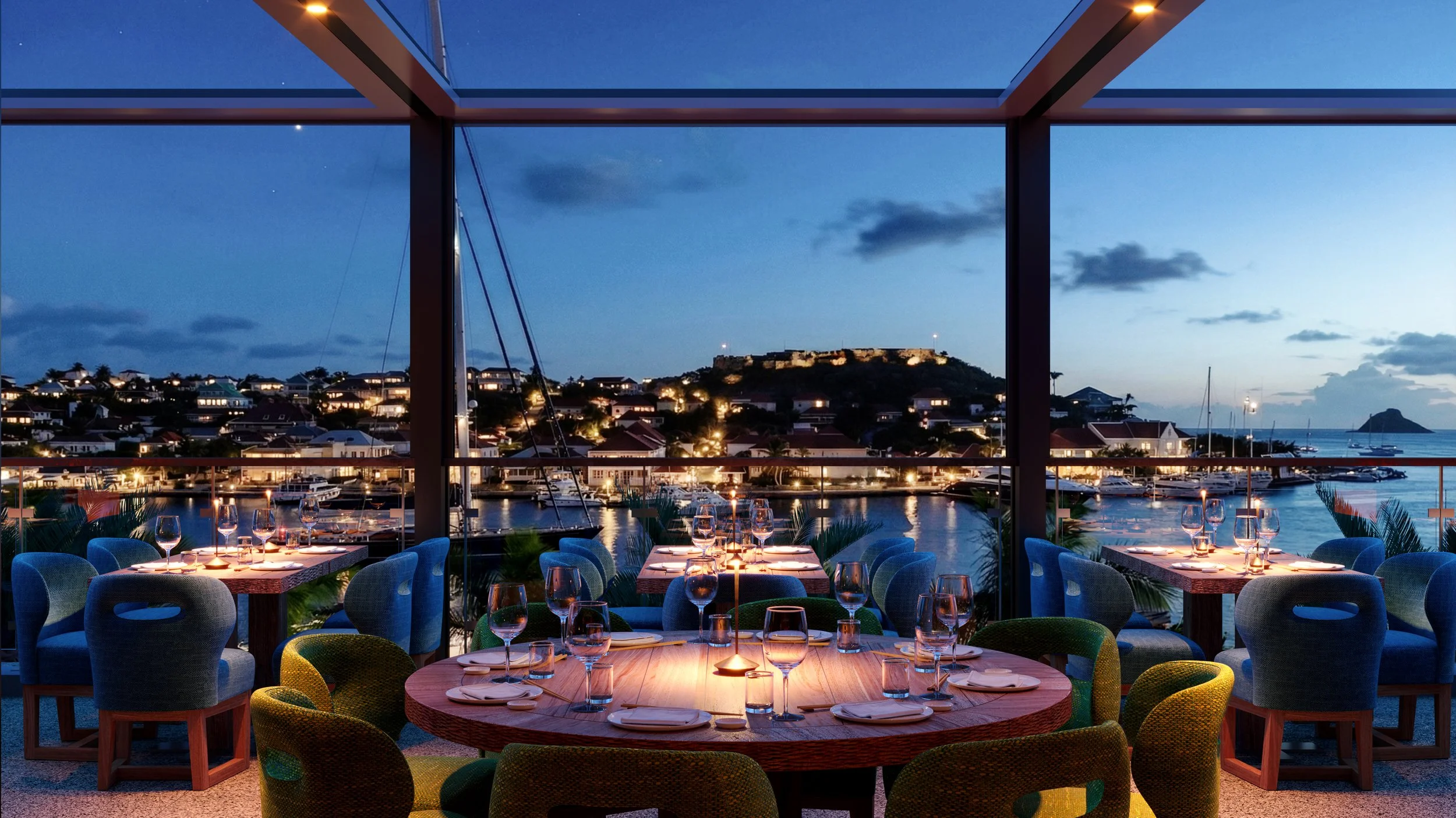A luxurious outdoor dining area overlooking a marina at dusk, with tables set with glasses and candles, framed by a modern structure with glass walls and a scenic view of water, boats, and a hillside in the background.