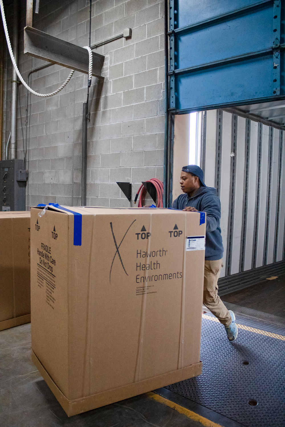 Worker moving a large Haworth Health Environments cardboard crate through a warehouse loading dock