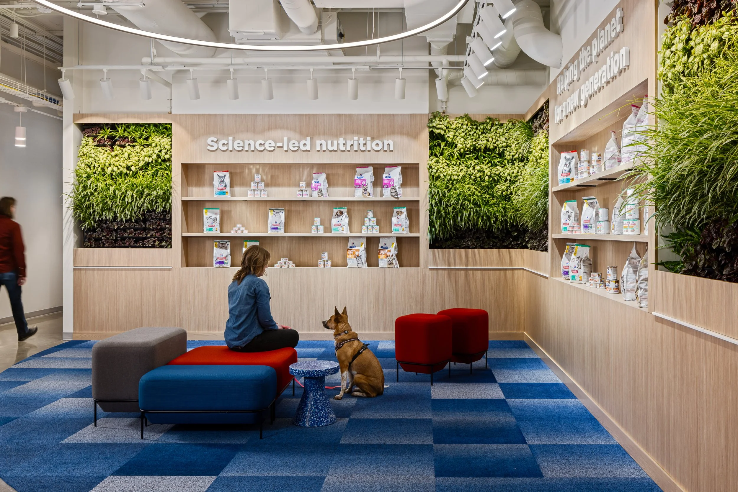 Modern pet nutrition showroom with dog food displays, living plant walls, and a woman sitting beside a dog