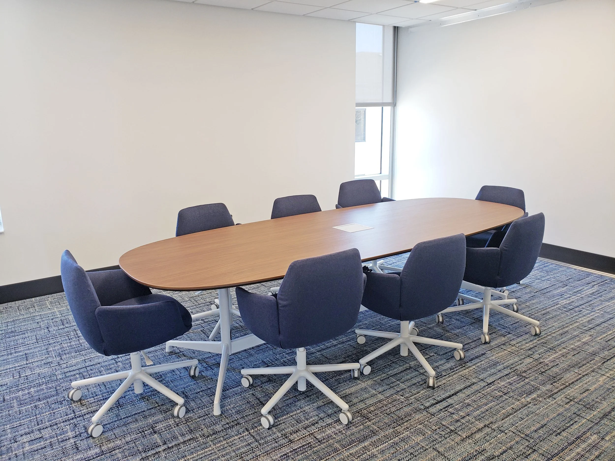 Modern conference room with a large oval wood table and navy rolling chairs