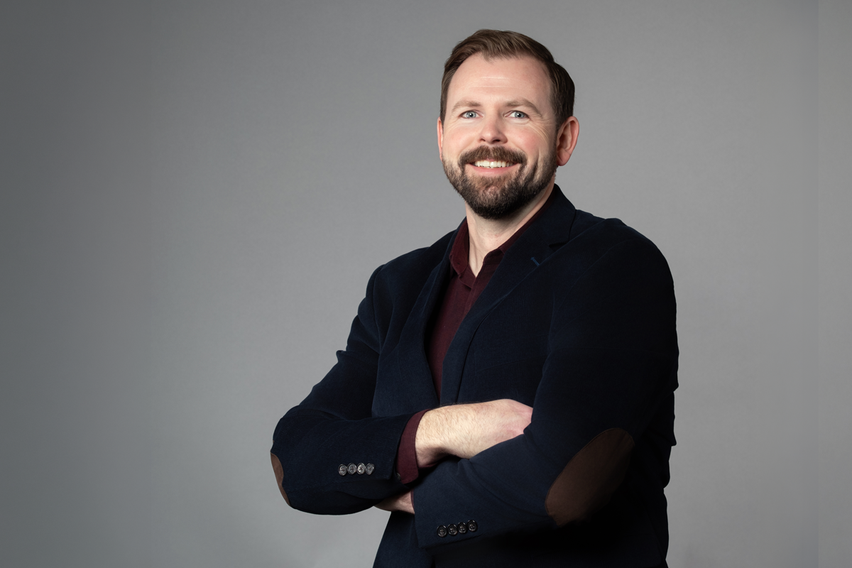 Matt Dunaway, promoted at encompas Installation Company eIC from Installation Manager to Installation Director in 2026. White man with brown trimmed beard standing with arms crossed, smiling and wearing a maroon shirt with a navy blazer.