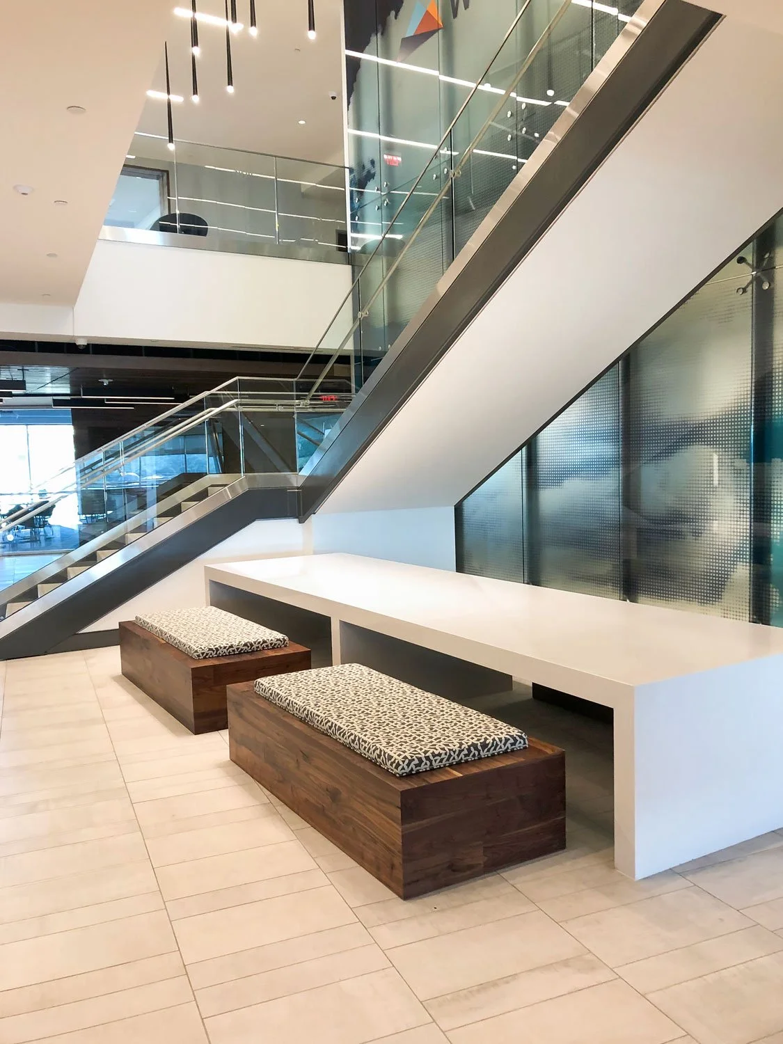 Modern office lobby with escalators, glass walls, patterned benches, and a long white counter