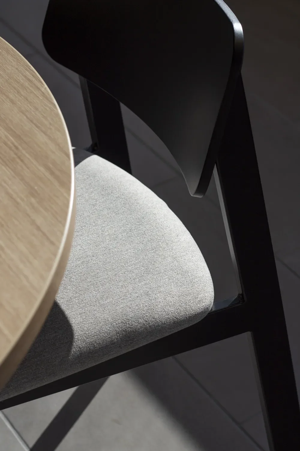 Close-up of a modern black dining chair with a light gray upholstered seat beside a round wooden table.