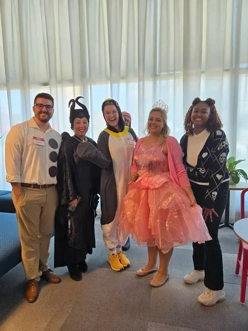 Group of five people in colorful costumes posing indoors by a window