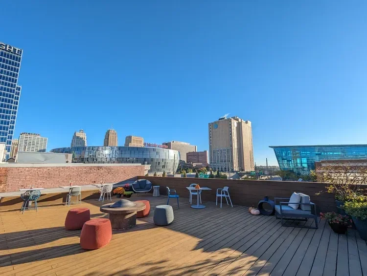 Rooftop terrace with outdoor seating and fire pit overlooking a downtown skyline under a clear blue sky