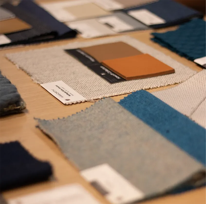 Fabric and upholstery swatches in neutral blue, gray, brown, and orange tones arranged on a tabletop